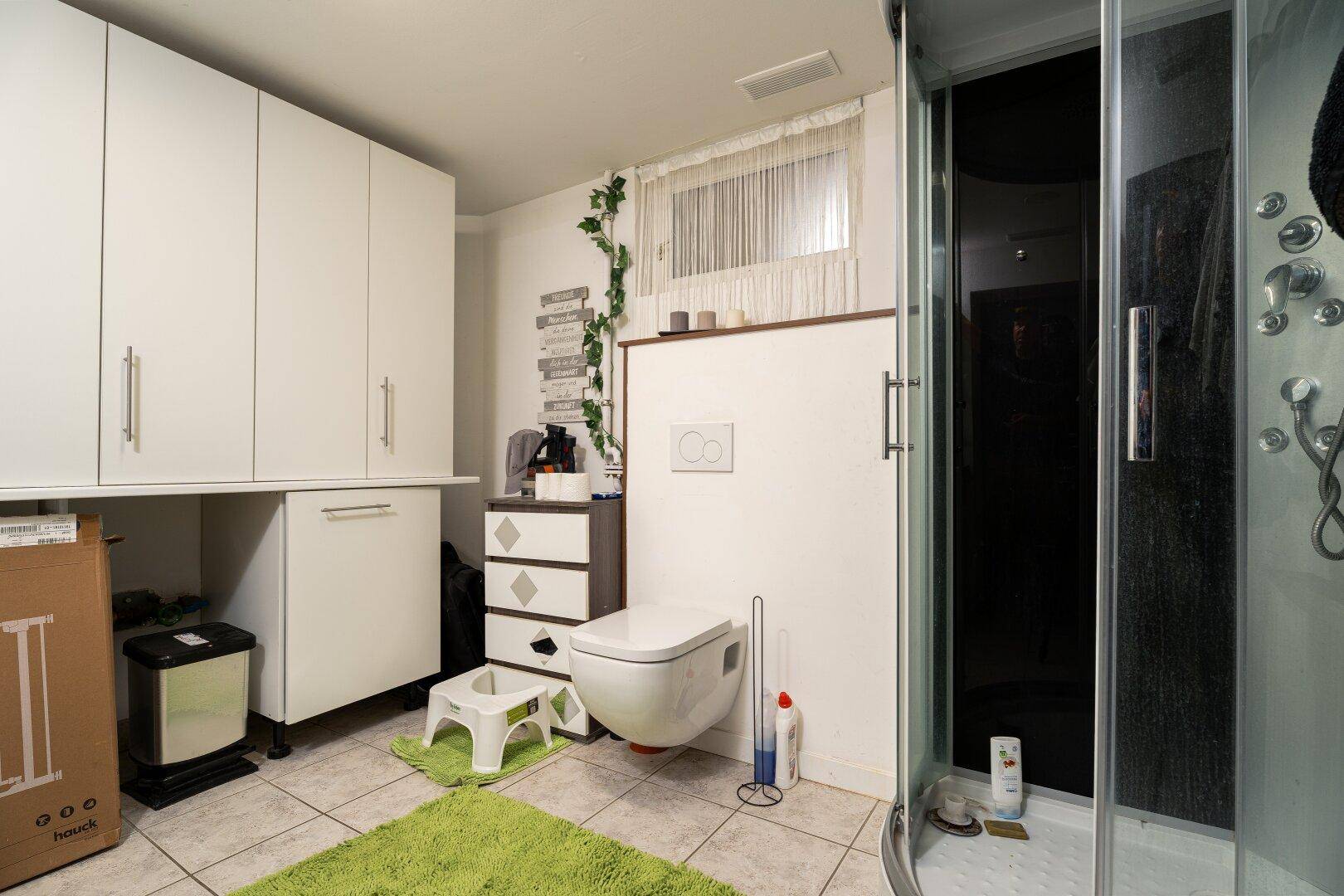Funktionales Badezimmer mit Duschkabine, WC und praktischen weißen Stauschränken.