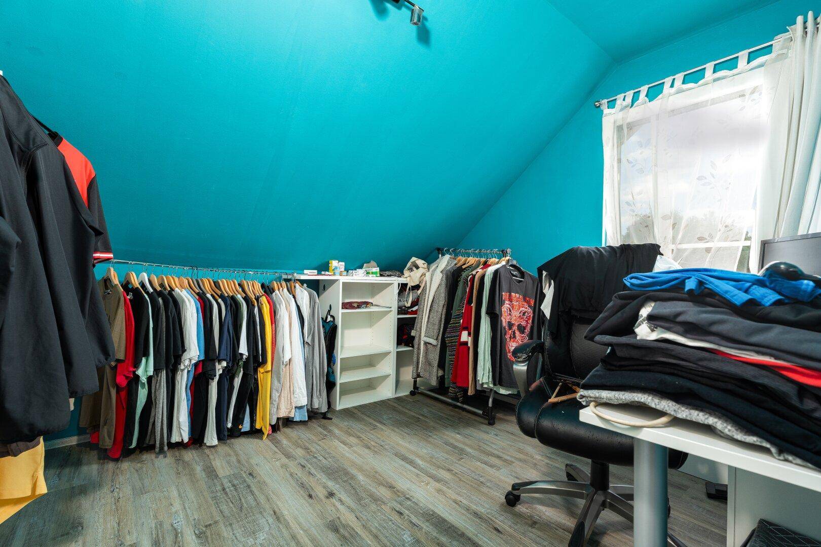 Dachschrägenzimmer mit leuchtend blauer Decke und offener Kleideraufbewahrung.