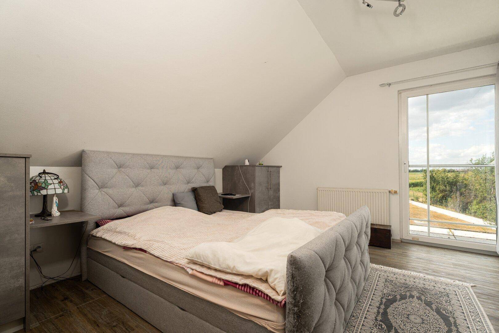 Helles Schlafzimmer mit großem Bett, Teppich und Balkontür mit Blick ins Grüne.