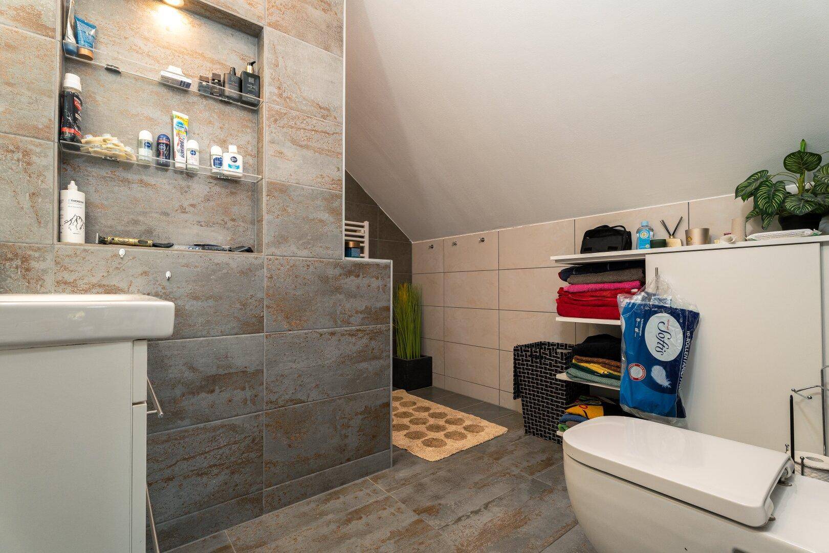 Modernes Badezimmer mit Fliesen, wandhängendem WC und praktischen Ablagen unter der Dachschräge.