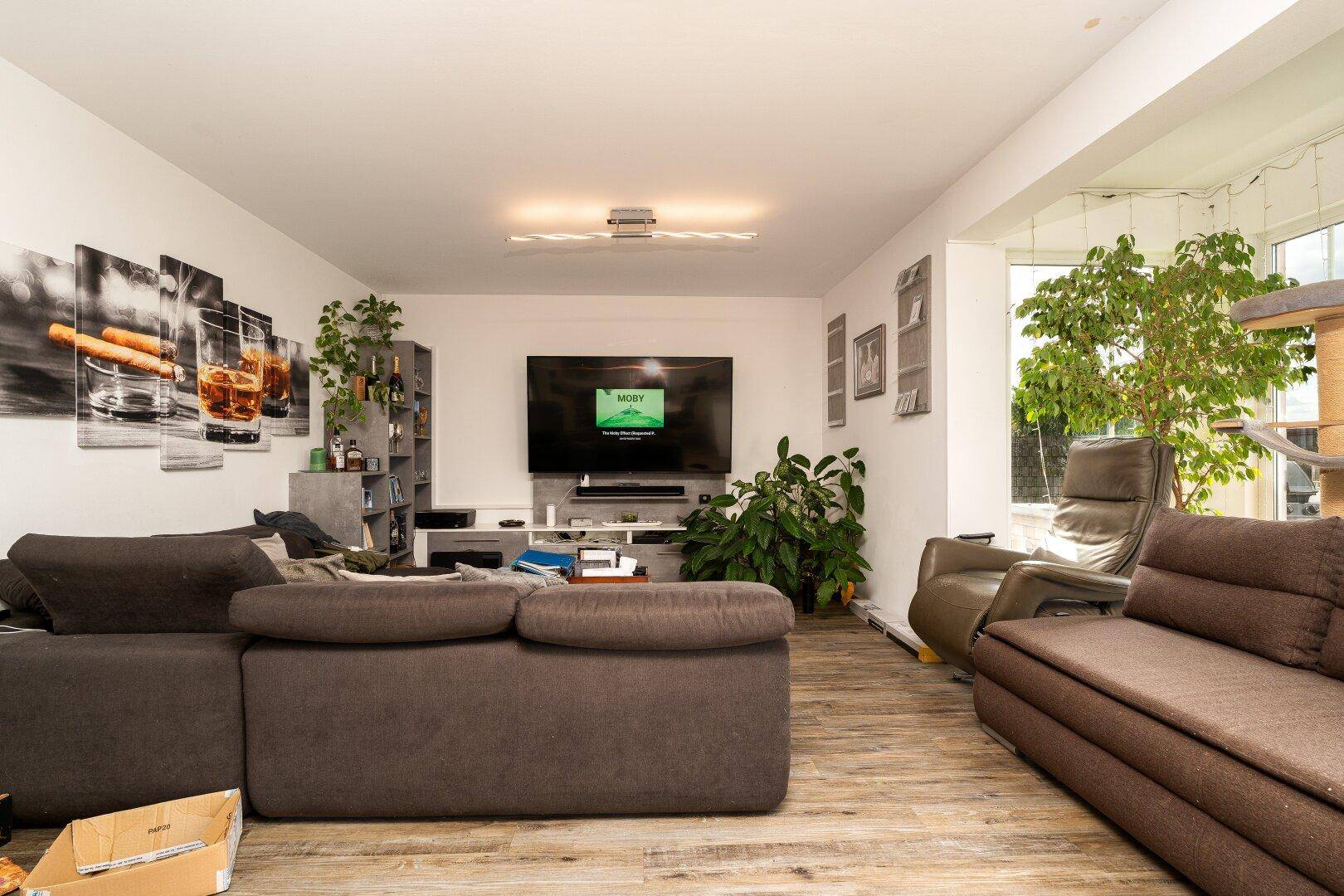 Gemütliches Wohnzimmer mit großem Sofa, Fernseher und hellem Wintergarten-Anbau.