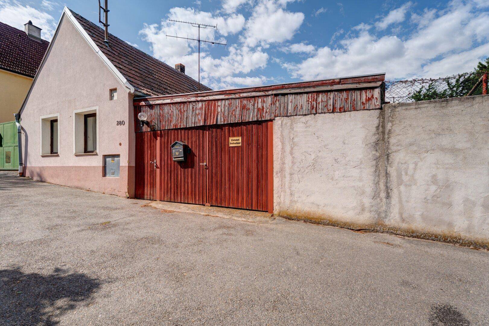 Fassade eines alten Hauses mit einer großen roten Holztür und einem Briefkasten unter blauem Himmel.