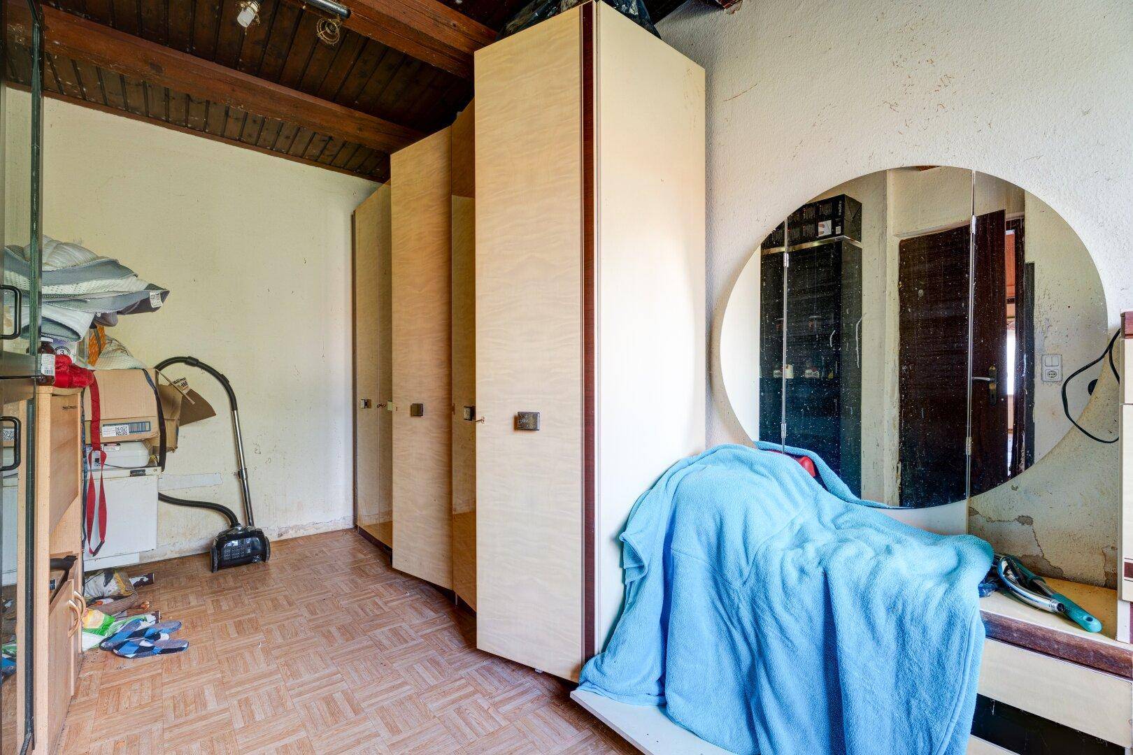 Schlafzimmer oder Abstellraum mit mehreren Kleiderschränken, einem runden Spiegel und Holzbalken.