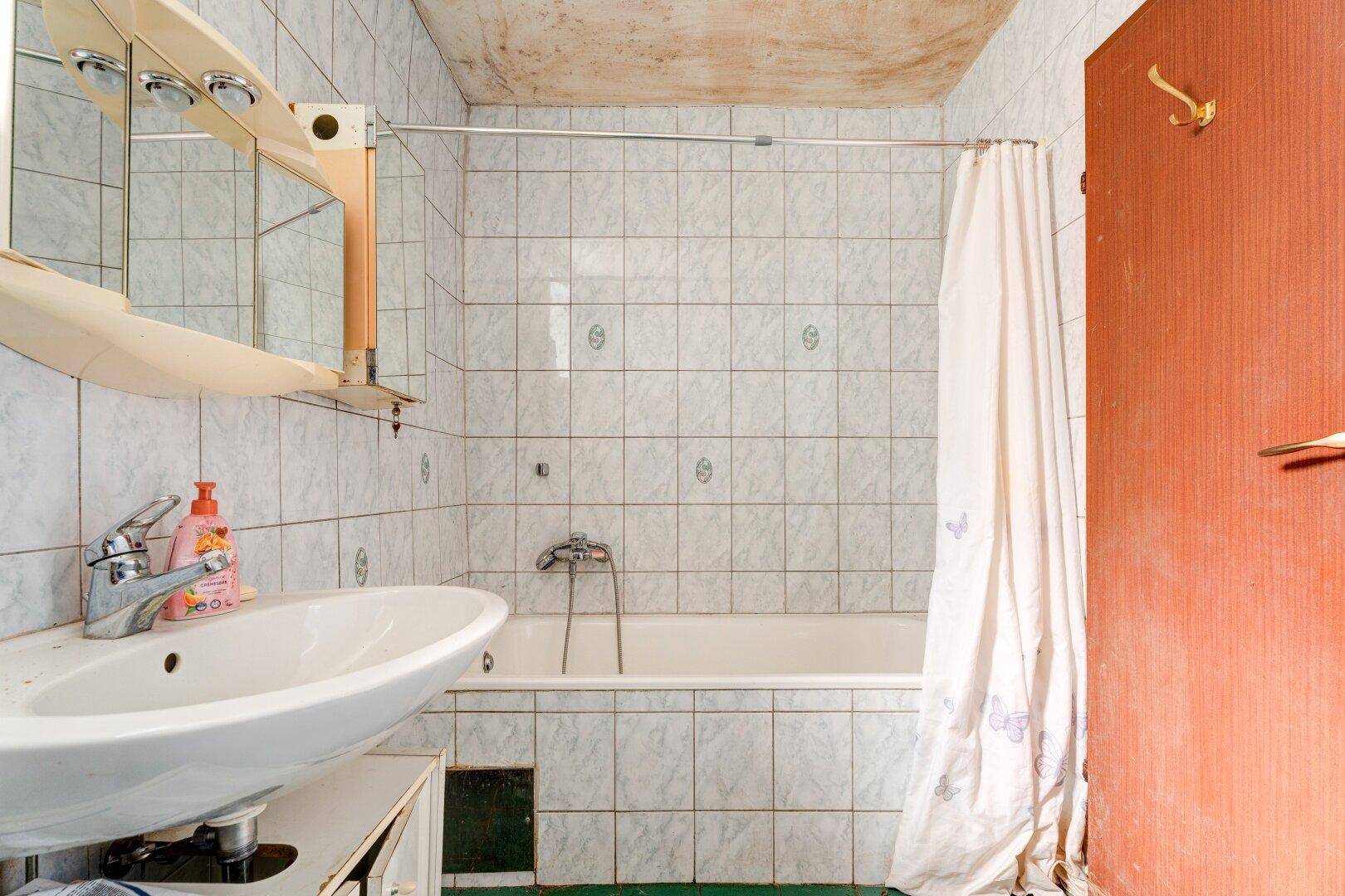 Badezimmer mit weiß gefliesten Wänden, Waschbecken und einer Badewanne mit Duschvorhang.