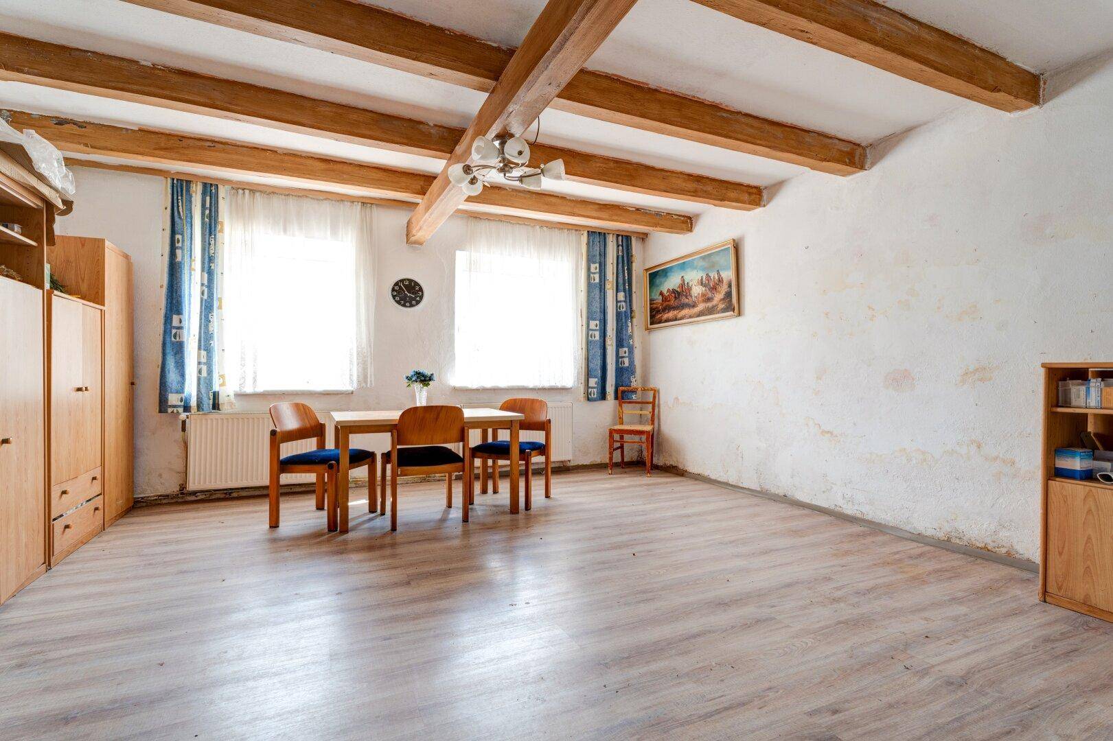 Wohn- und Essbereich mit sichtbaren Holzbalken, Laminatboden und einem Esstisch am Fenster.