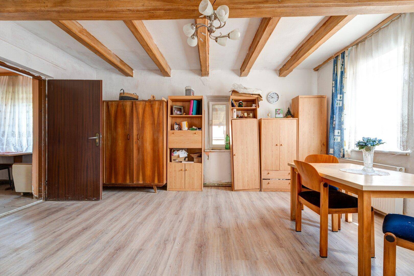 Geräumiger Wohn- und Essbereich mit Holzbalken, Laminatboden und verschiedenen Holzmöbeln.