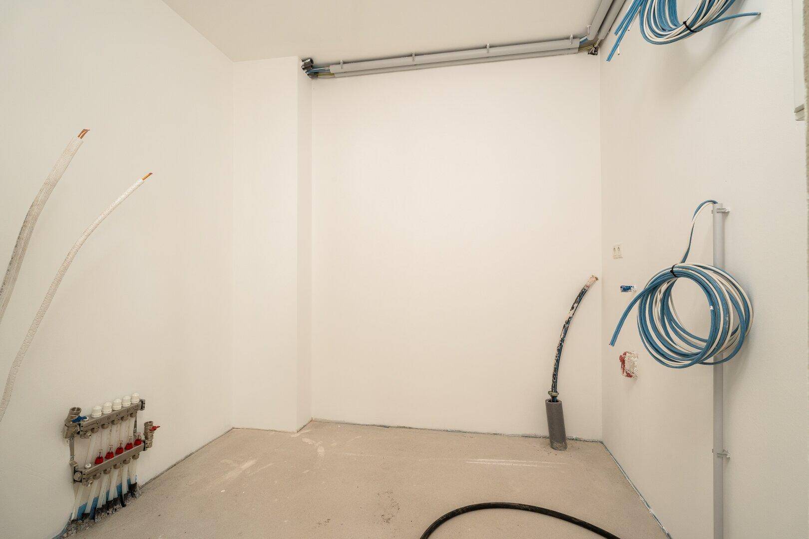 Unfertiger Technikraum mit sichtbaren Rohrleitungen und Installationen für die Haustechnik.