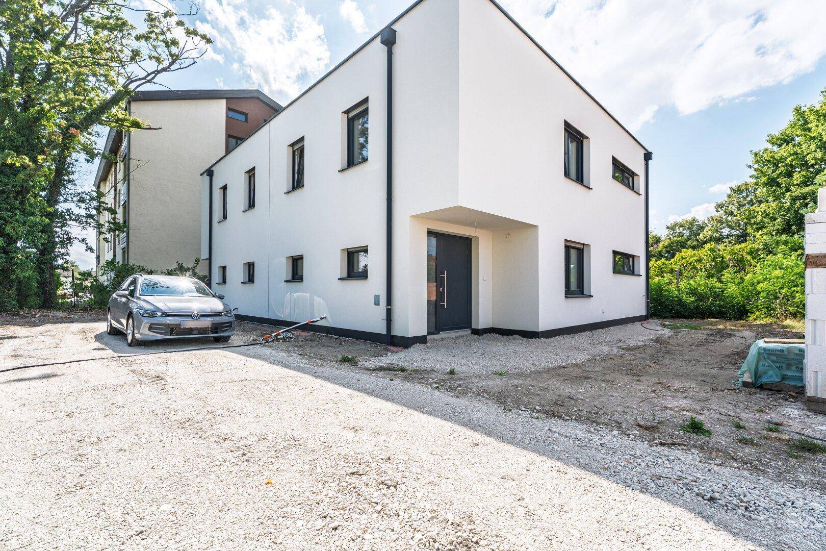 Vorderansicht eines modernen Einfamilienhauses mit weißer Fassade, dunkler Eingangstür und Kiesauffahrt.