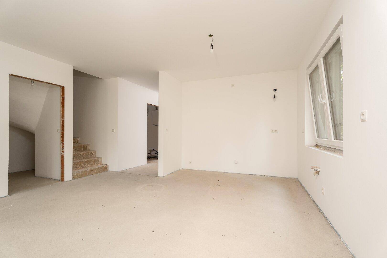 Heller, unfertiger Wohnbereich mit Treppenaufgang und großen Fenstern, bereit für den Innenausbau.