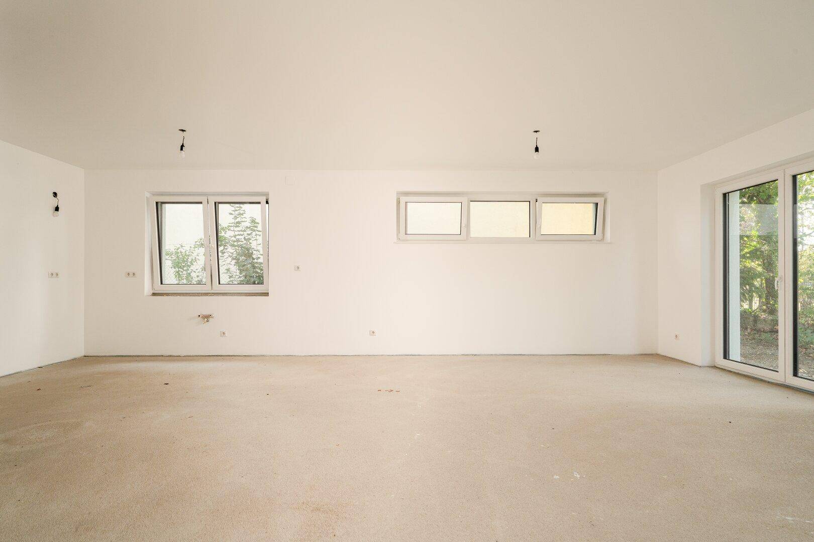Geräumiger, unfertiger Wohnraum mit mehreren Fenstern, der viel natürliches Licht hereinlässt.