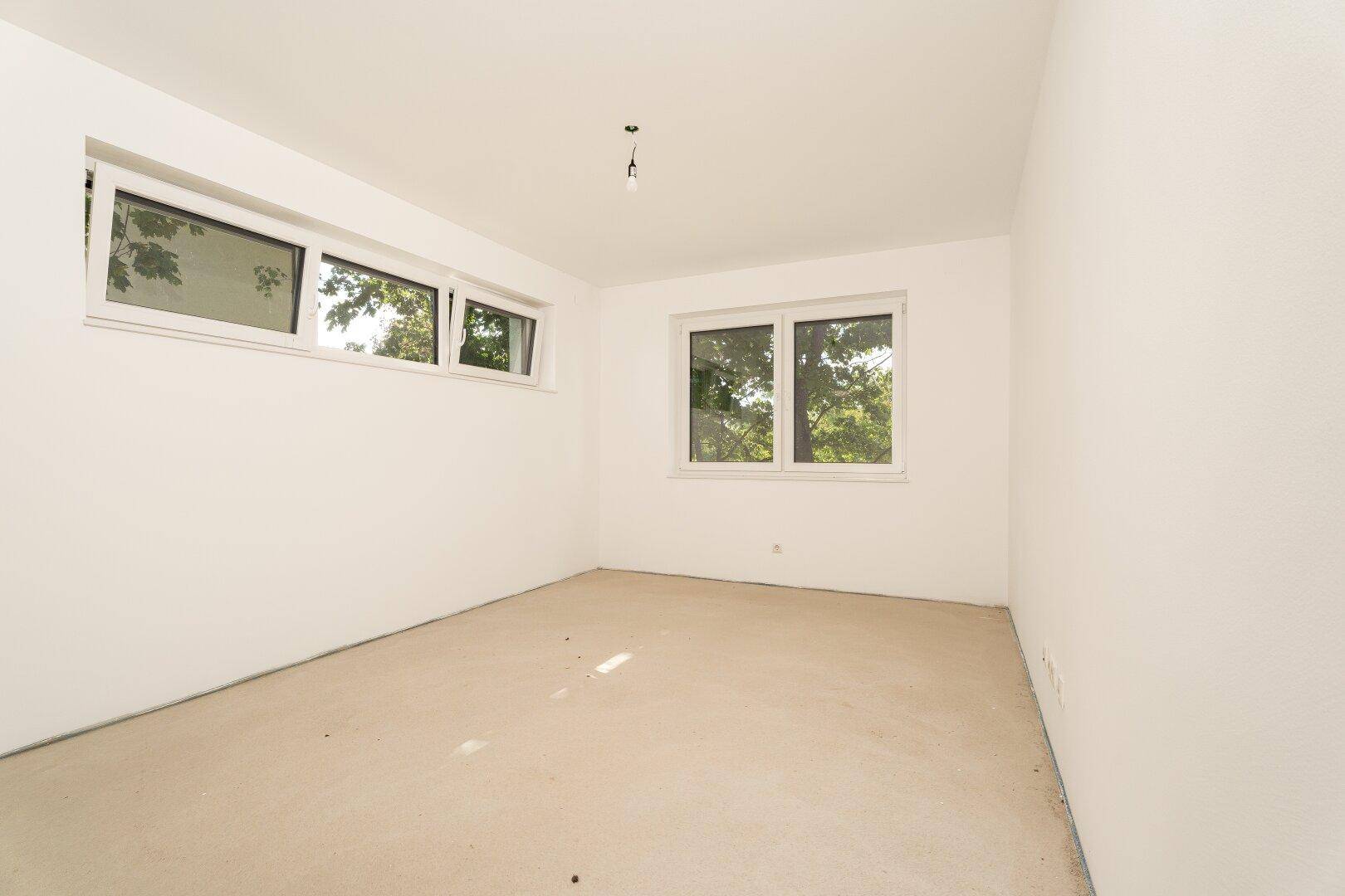 Helles, unfertiges Schlafzimmer mit zwei Fenstern, bereit für den Innenausbau und die Einrichtung.