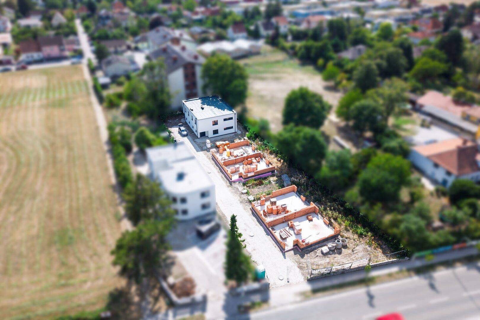 Weitläufige Luftaufnahme einer Wohnsiedlung mit Neubauten und mehreren Baustellen in grüner, ländlicher Umgebung.