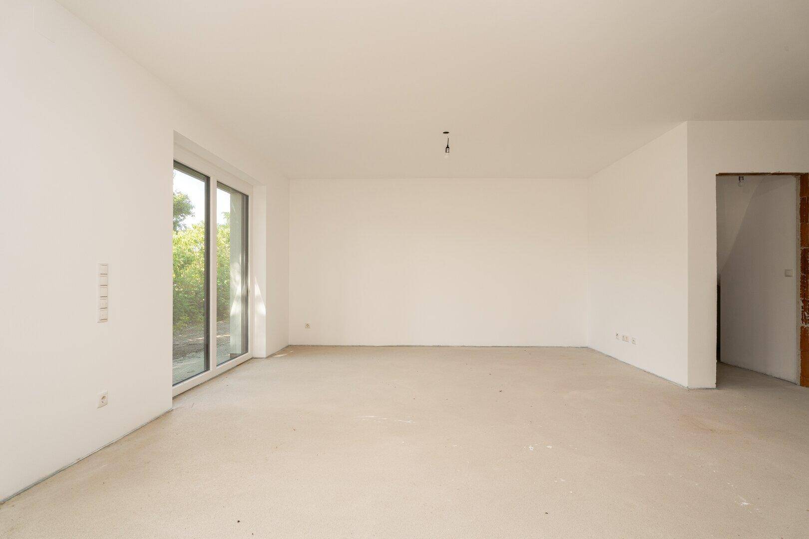 Heller, leerer Wohnraum im Neubau mit großen Fenstern und Rohbauzustand, bereit für den Innenausbau.