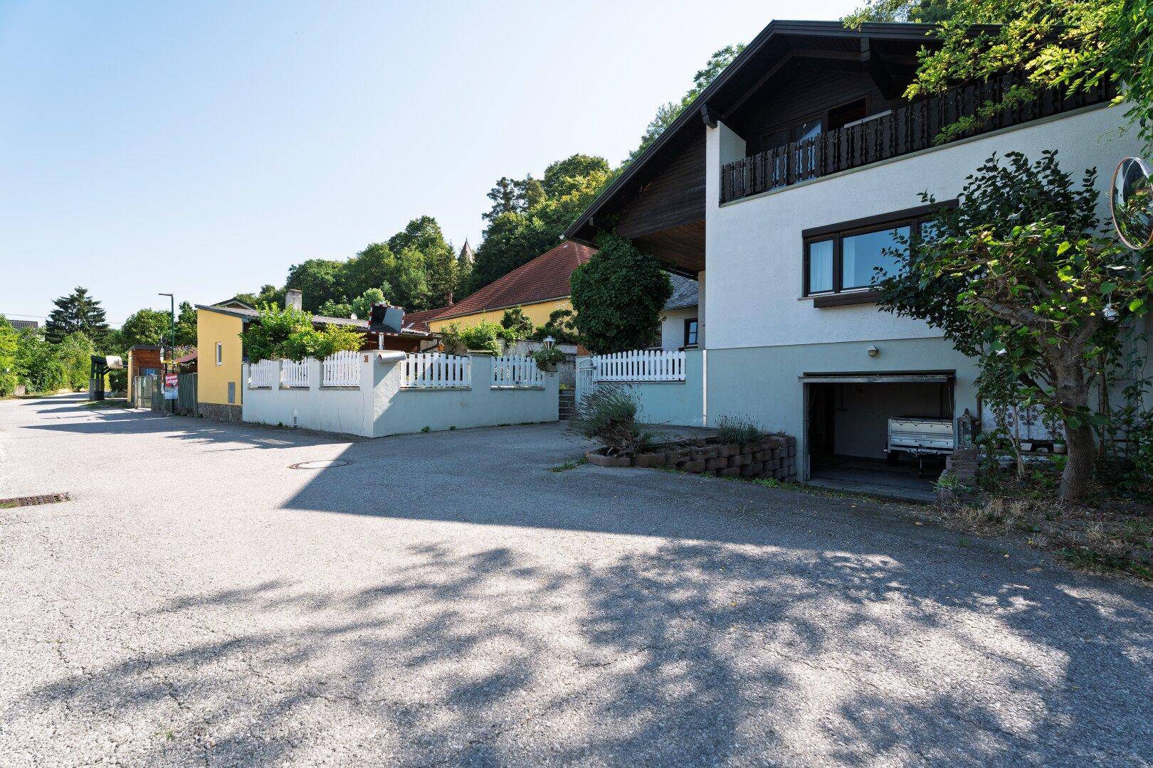 Seitenansicht des Hauses mit Einfahrt und integrierter Garage, umgeben von üppigem Grün.