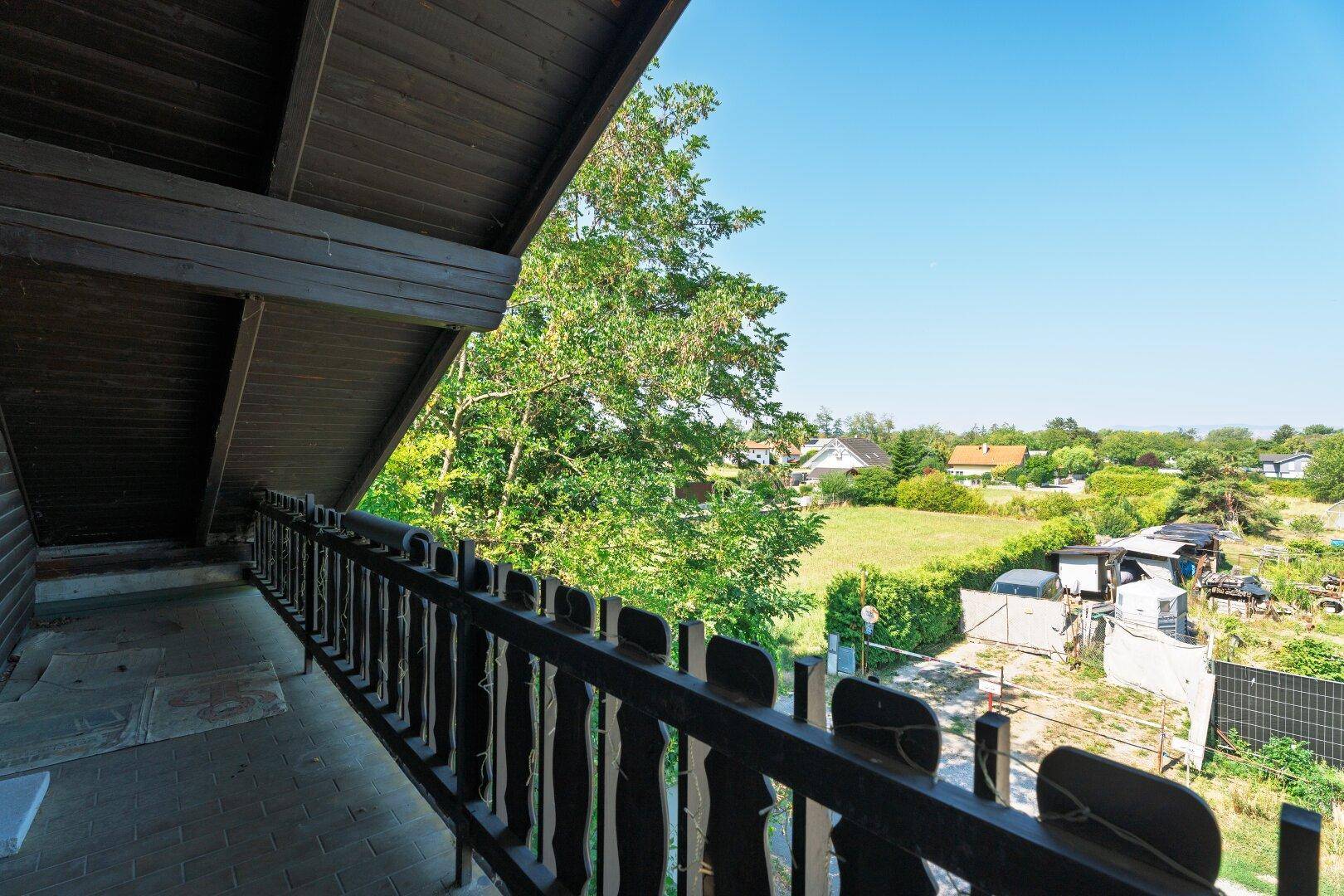 Balkon mit Holzbalken und Blick auf die ländliche Umgebung und Gärten.