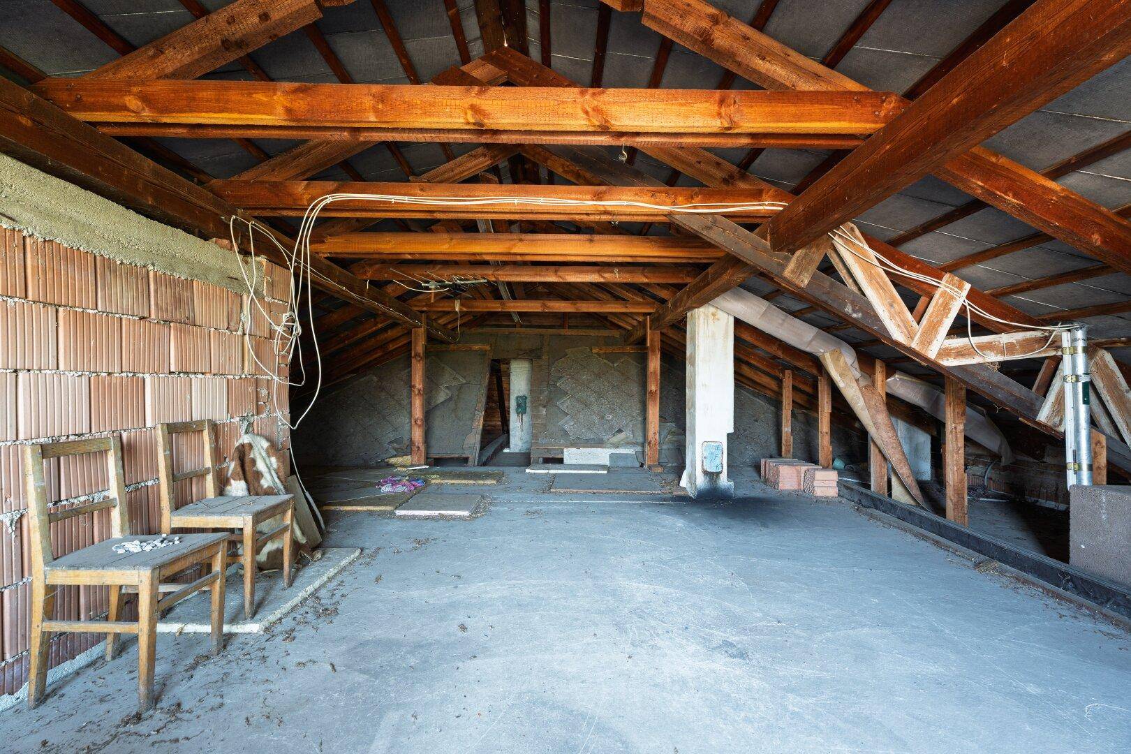 Unausgebauter Dachboden mit sichtbaren Holzbalken und Ziegelwänden, bietet Potenzial für zukünftige Nutzung.