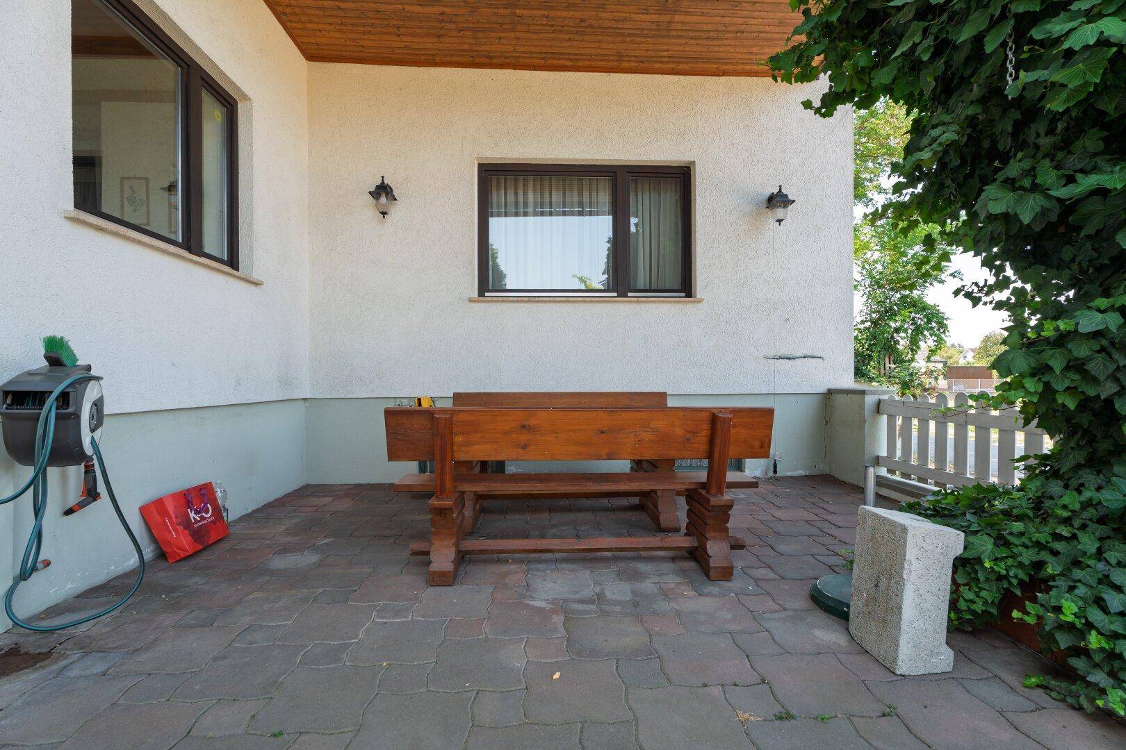 Gepflasterte Terrasse mit rustikalem Holztisch und Sitzgelegenheiten, umgeben von Grün.