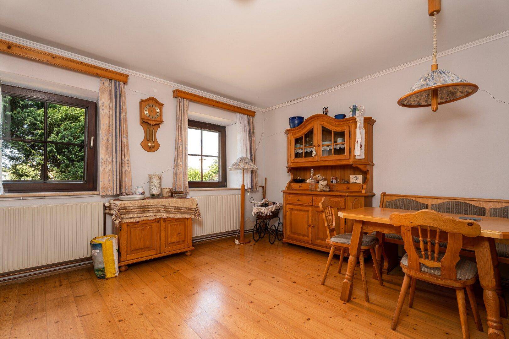 Essbereich mit Holztisch und Stühlen, umgeben von traditionellen Holzschränken und Fenstern.