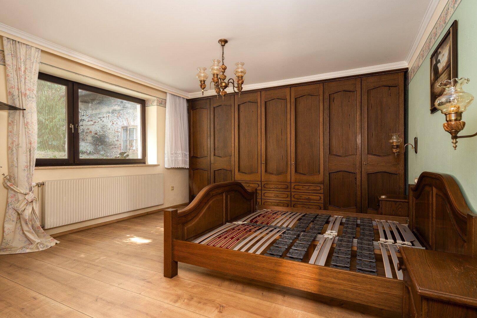 Schlafzimmer mit Holzbett, Einbauschränken und Holzboden, hell durch großes Fenster.