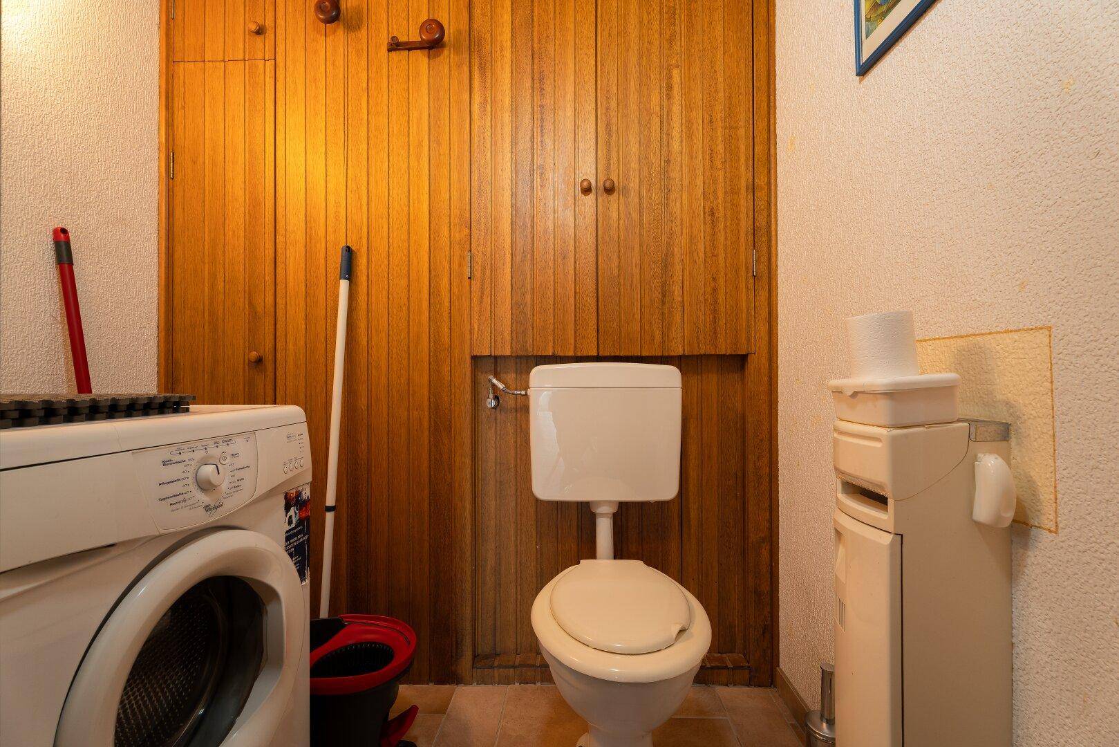 Kleiner WC-Raum mit Toilette, Waschmaschine und Holzverkleidung an der Wand.