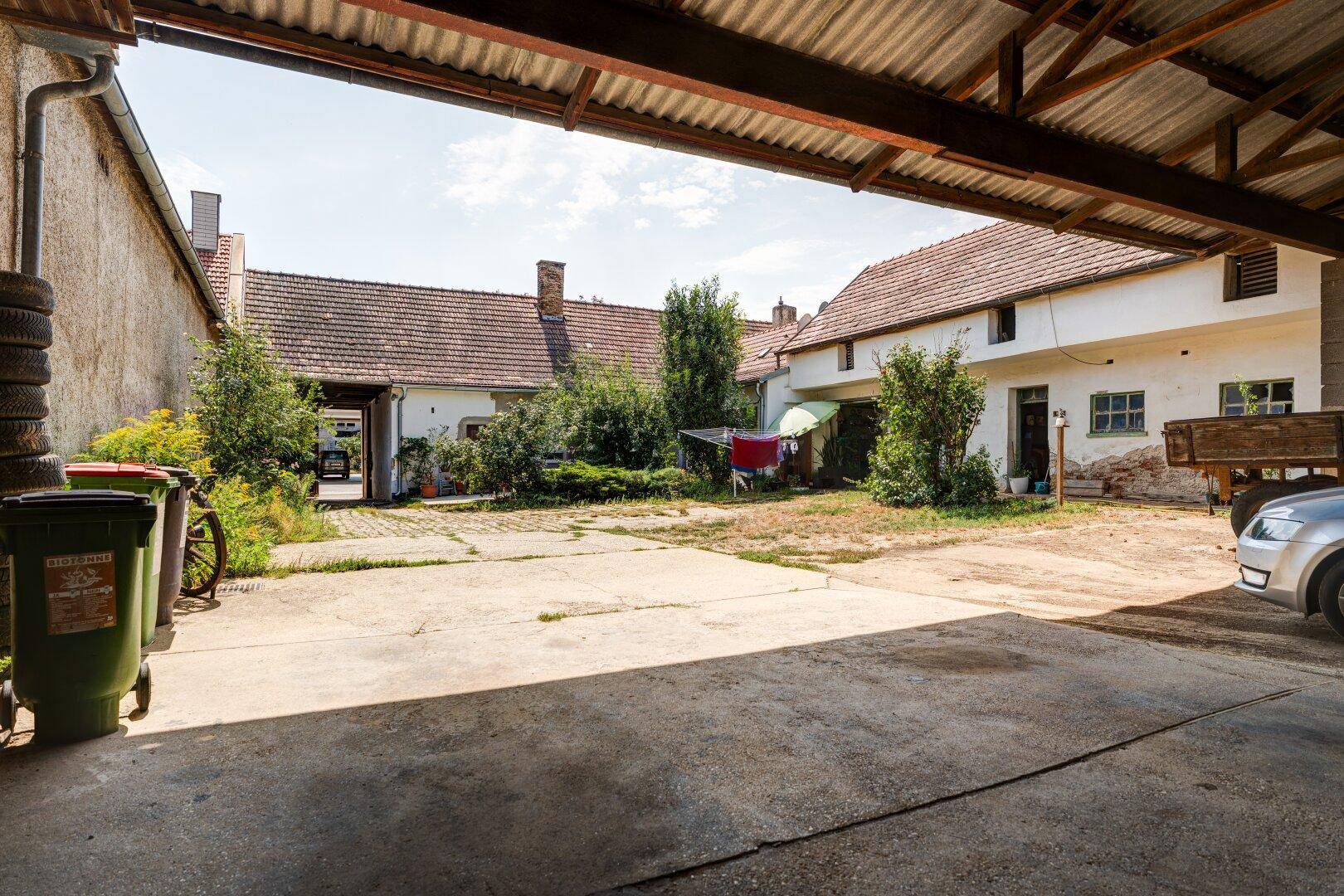 Großer Innenhof mit Betonfläche, umgeben von mehreren Gebäuden und viel Grün, das eine ländliche Atmosphäre schafft.