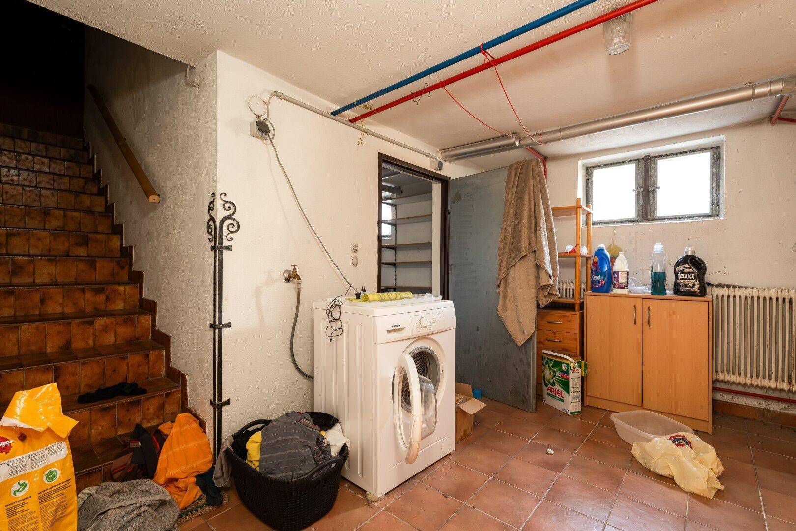 Waschküche im Keller mit Waschmaschine, Spülbecken und Treppenzugang, sehr funktional.