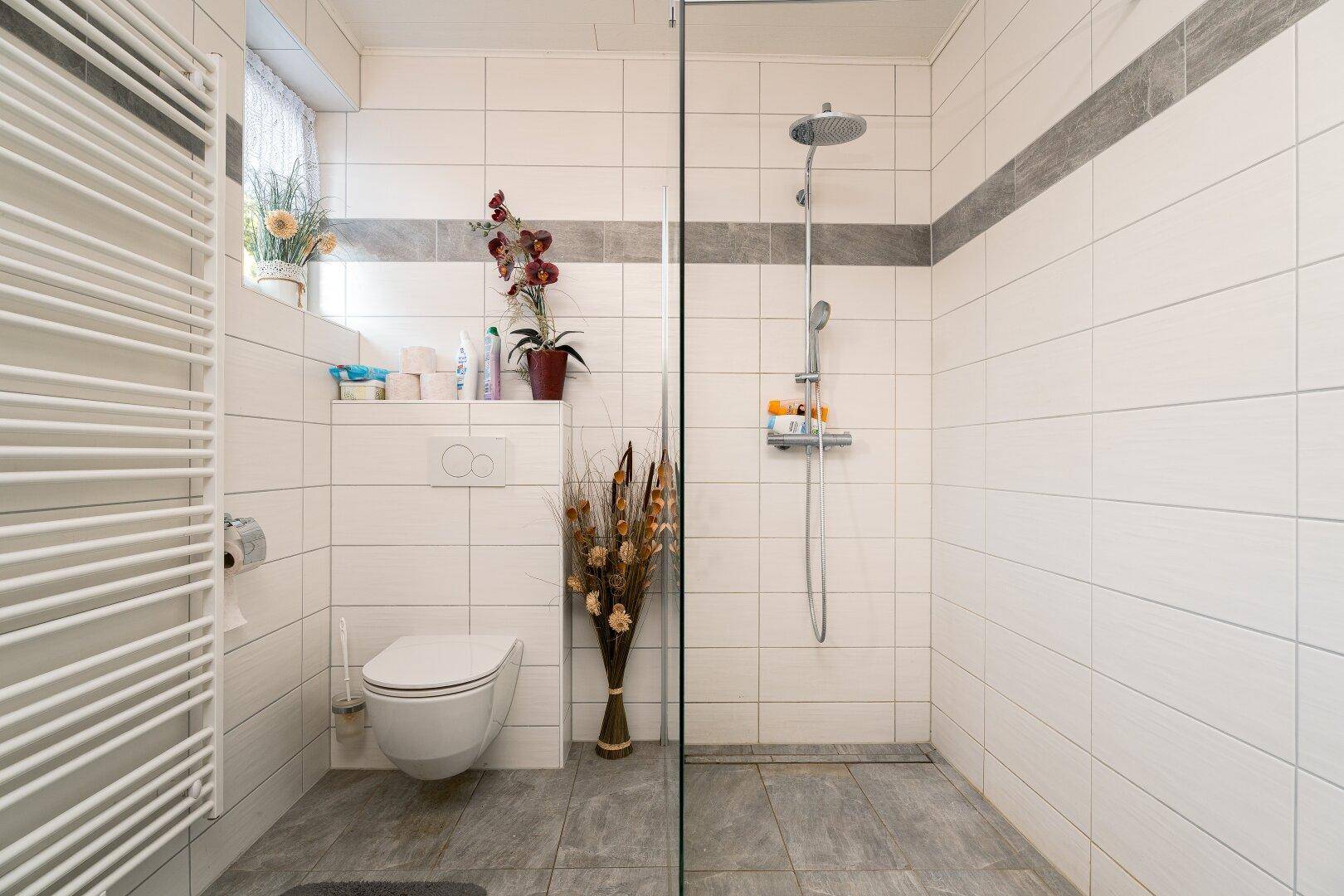 Helles Badezimmer mit ebenerdiger Dusche, Wand-WC und Handtuchheizkörper in modernem Design.