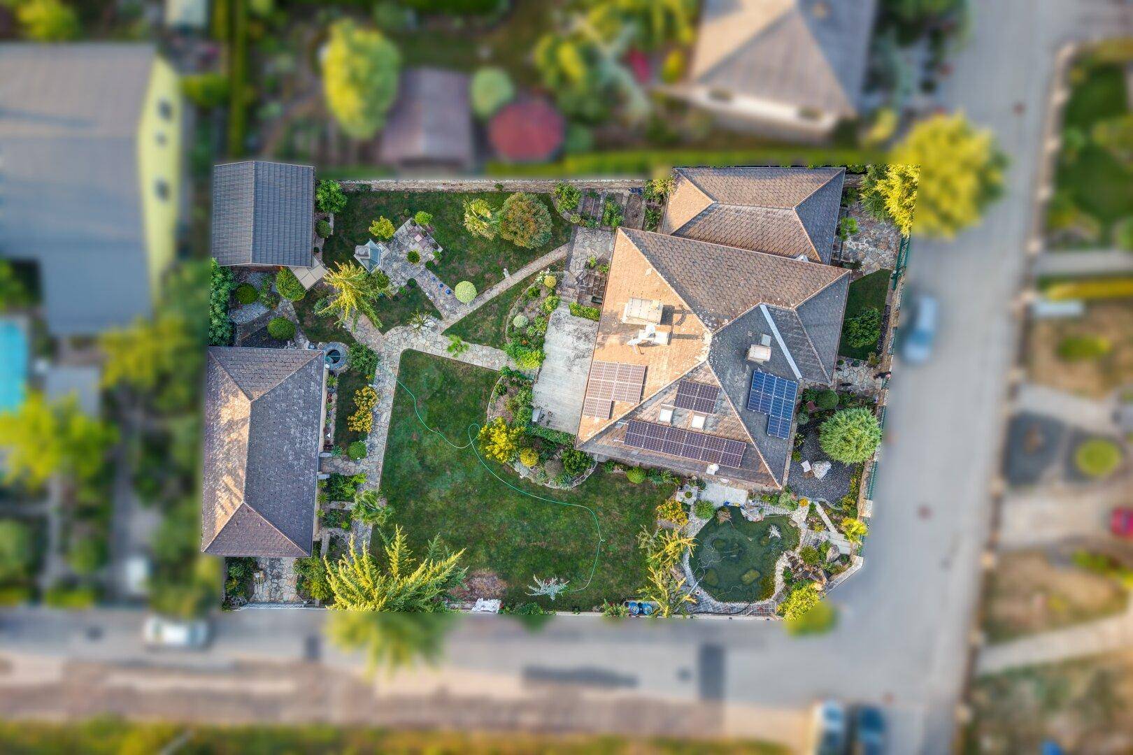 Draufsicht auf ein Wohnhaus mit großem Garten, Teich und Photovoltaikmodulen auf dem Dach.