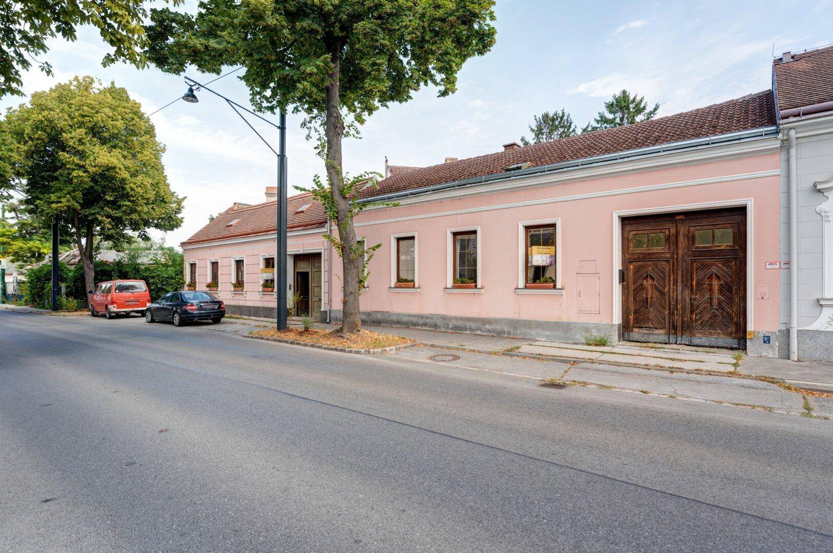 Historische Fassade des Gebäudes mit rosa Anstrich, traditionellen Fenstern und großen Holztoren.