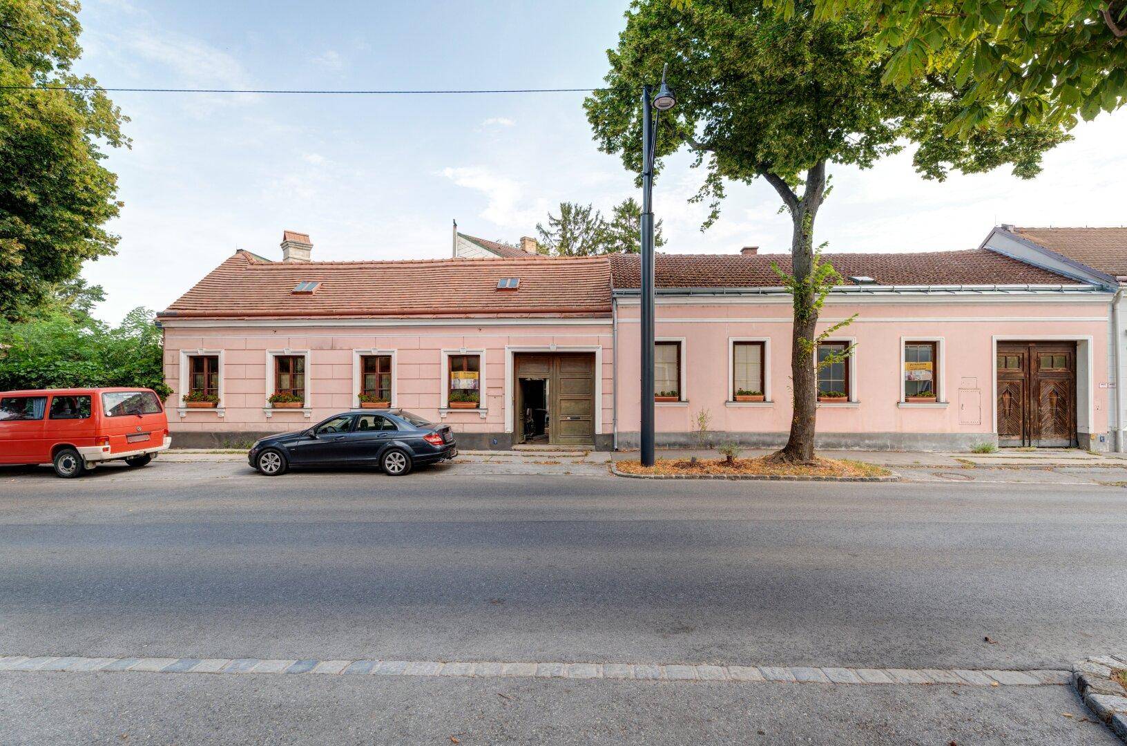 Ansicht der rosa gestrichenen Hausfassade mit traditionellen Fenstern und rustikalen Holztoren an der Straße.