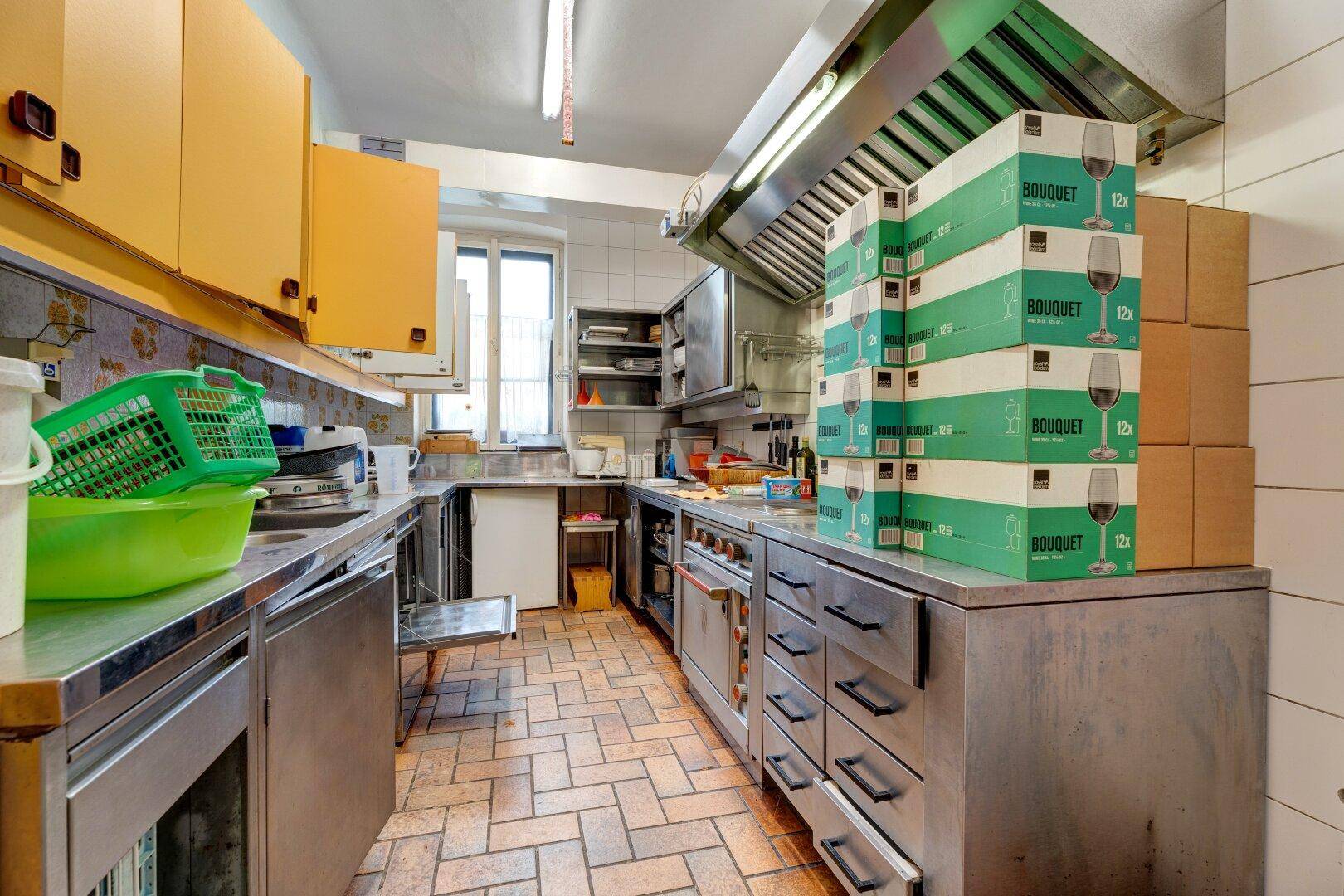 Professionelle Küche mit Edelstahloberflächen, Dunstabzugshaube und gelben Oberschränken für den Gastronomiebetrieb.