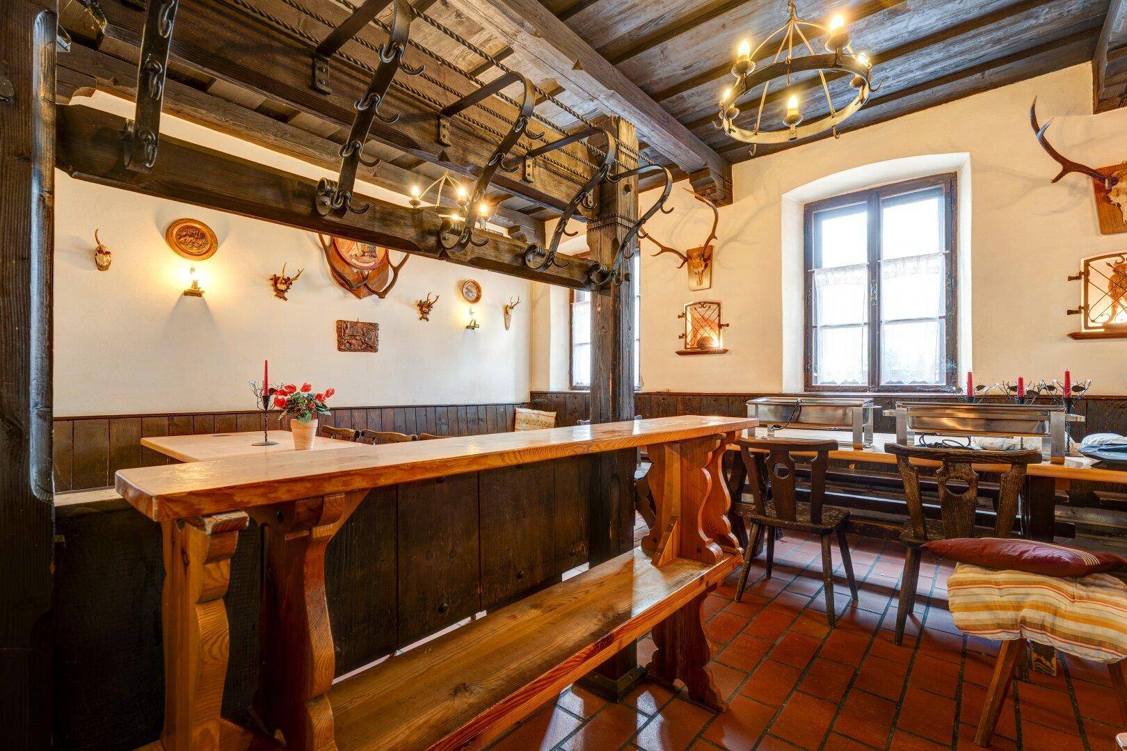 Gemütlicher Essbereich im Landhausstil mit Holztischen, Bänken und Hirschgeweihen an den Wänden.