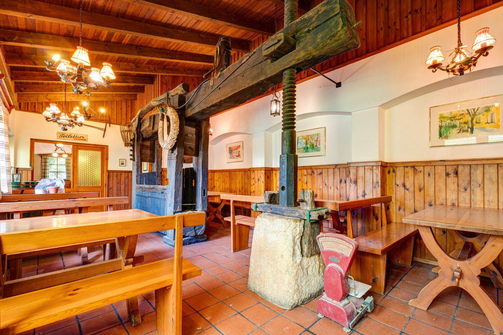 Historischer Gastraum mit einer alten Weinpresse, Holztischen und Bänken, die eine besondere Atmosphäre schaffen.