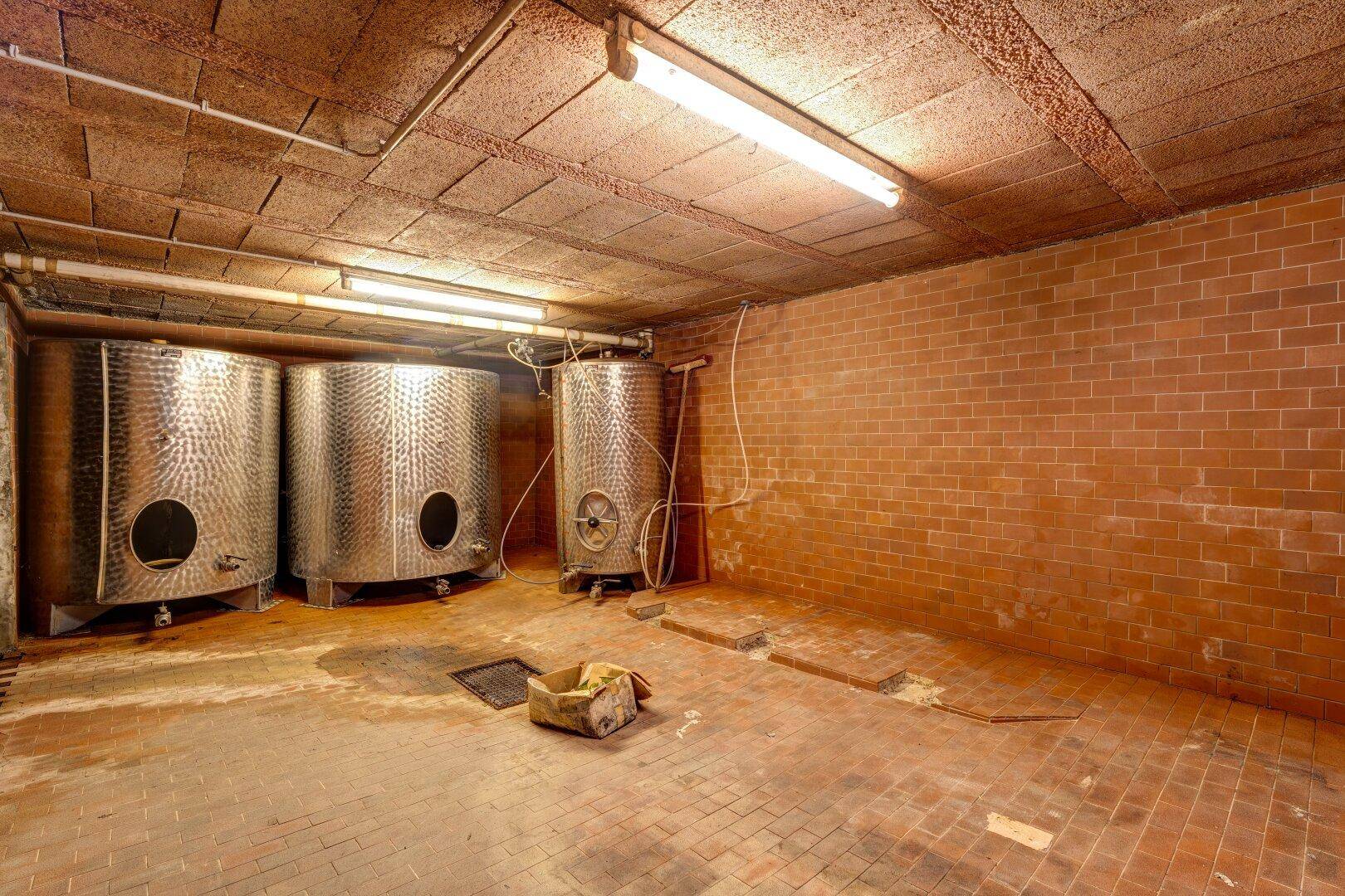 Kellerraum mit Ziegelwänden, Ziegelboden und großen Edelstahltanks, ideal für Weinlagerung.