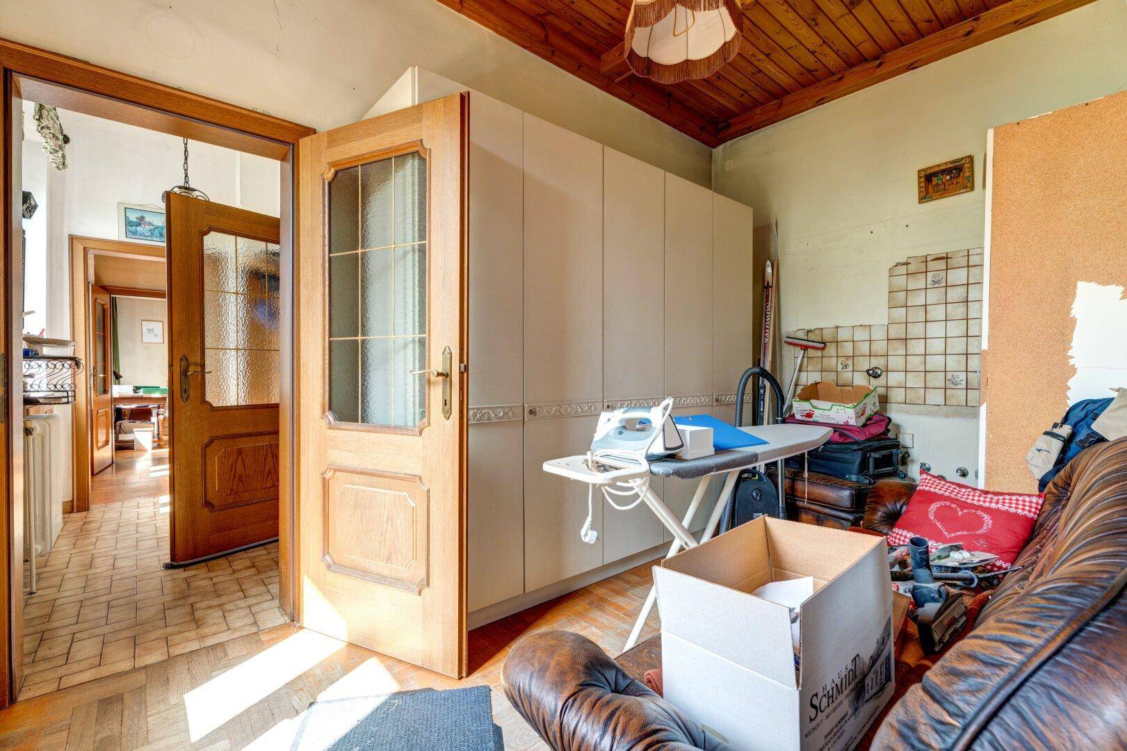 Hauswirtschaftsraum mit Bügelbrett, Schränken und einem Ledersofa, der viel Stauraum bietet.