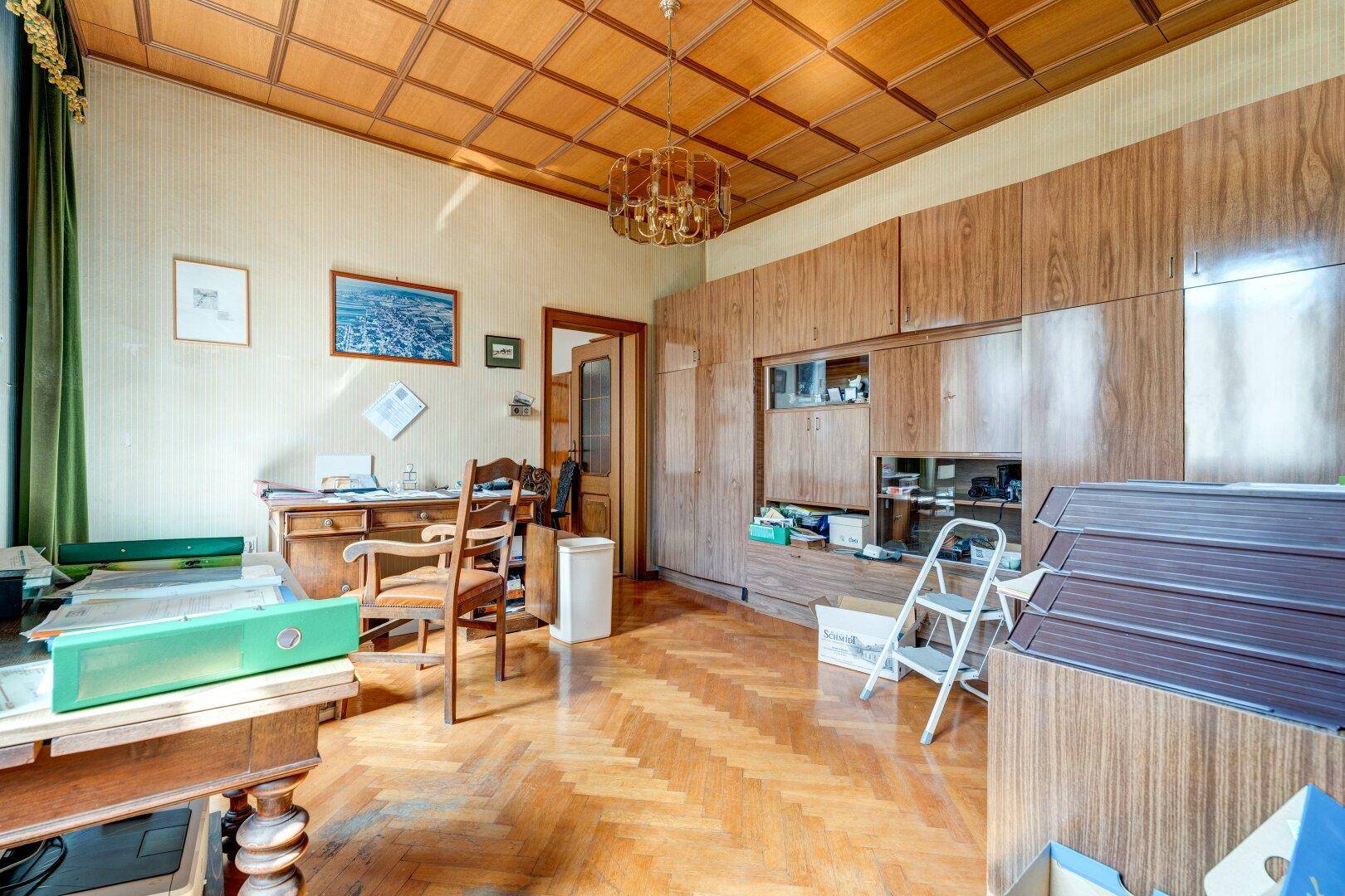 Geräumiges Büro mit Holzvertäfelung, Kassettendecke und Fischgrätparkett.