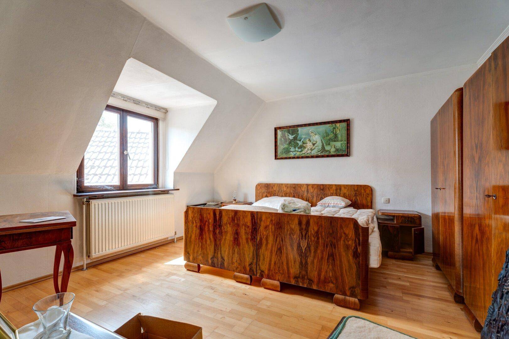 Schlafzimmer im Dachgeschoss mit Holzboden, Dachschräge und antiken Holzmöbeln.