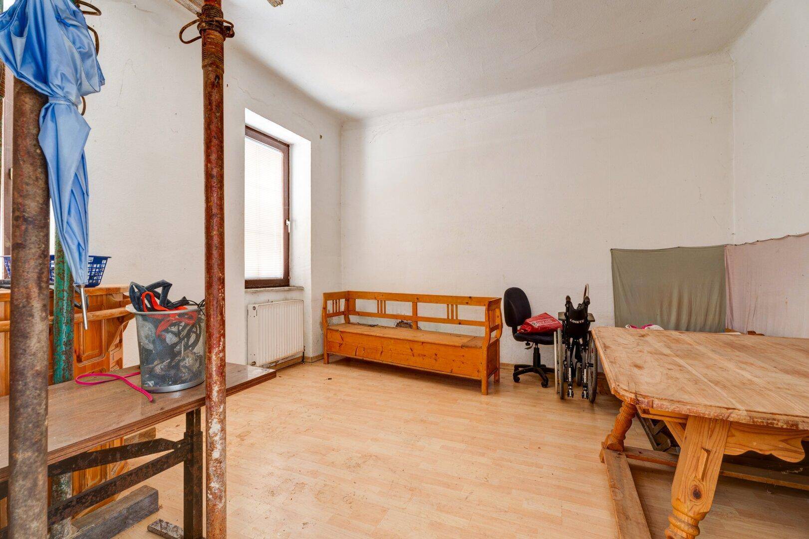 Großer Raum mit Holzboden, Fenster und provisorischen Stützen, der als Lager dient.