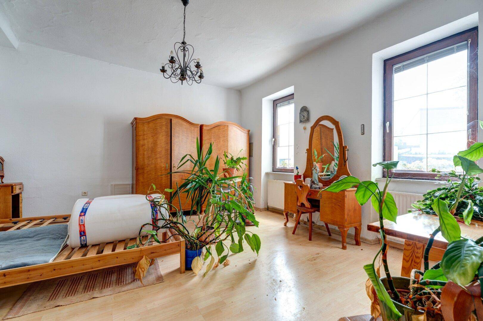 Helles Schlafzimmer mit Holzboden, großen Fenstern und antiken Holzmöbeln.