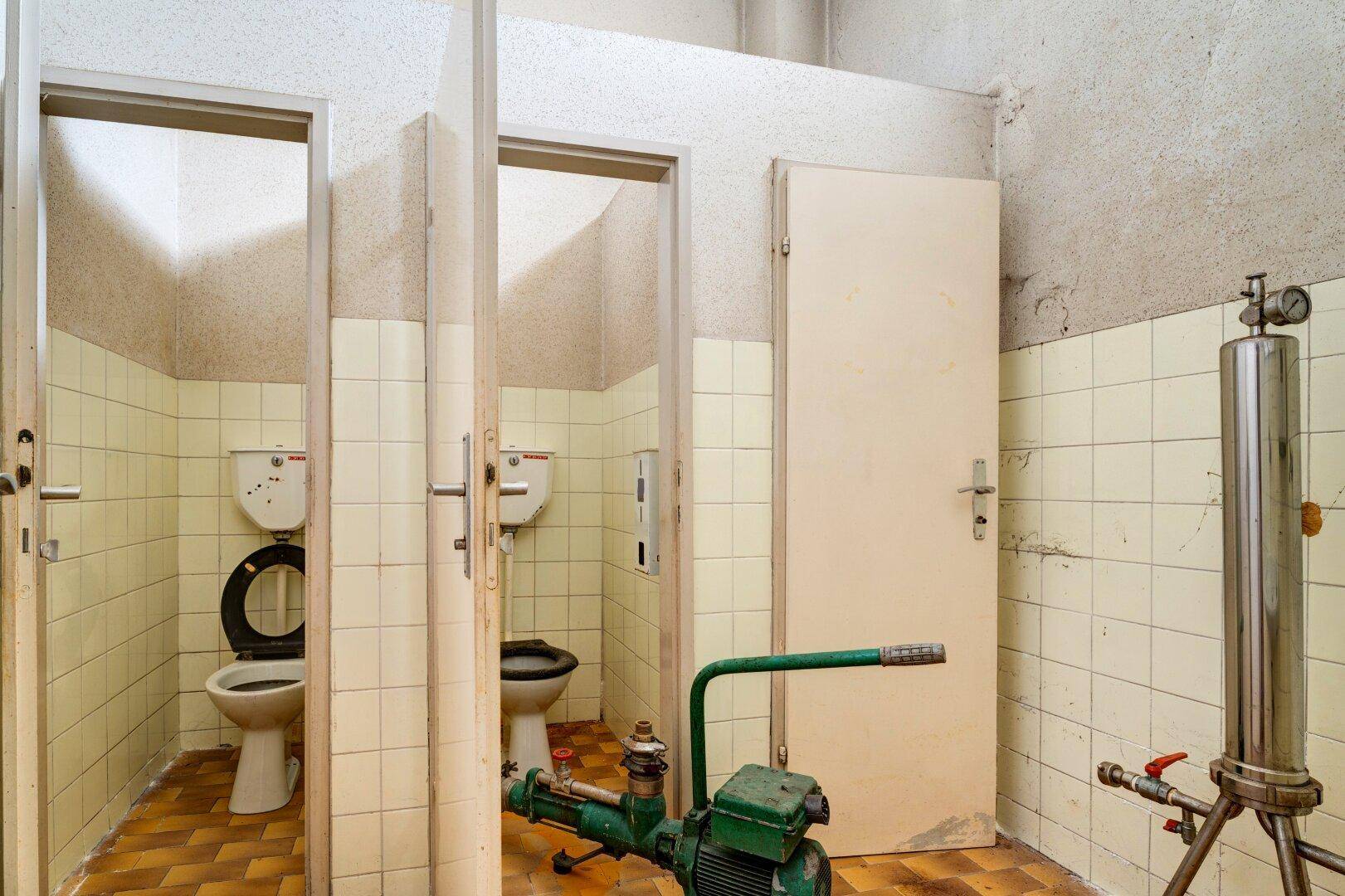 Mehrere Toilettenkabinen mit Fliesenboden und einfacher Ausstattung.