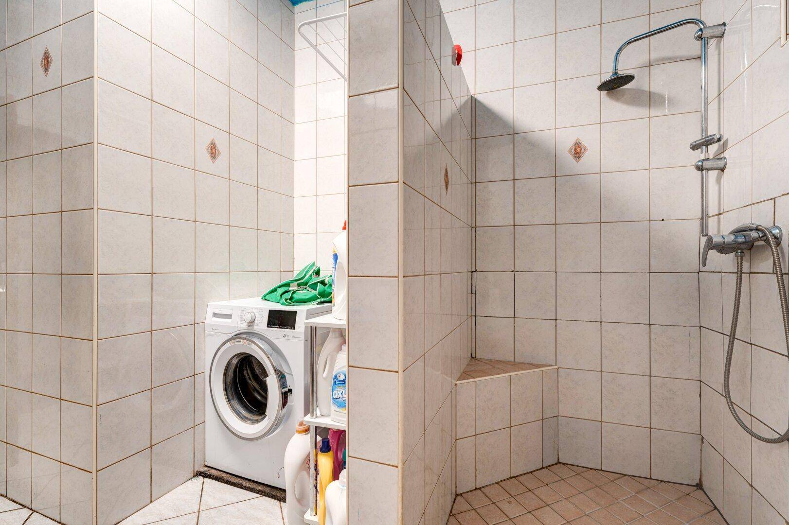 Duschbereich im Badezimmer mit Fliesen, Duschkopf und angrenzender Waschmaschine, praktisch gestaltet.
