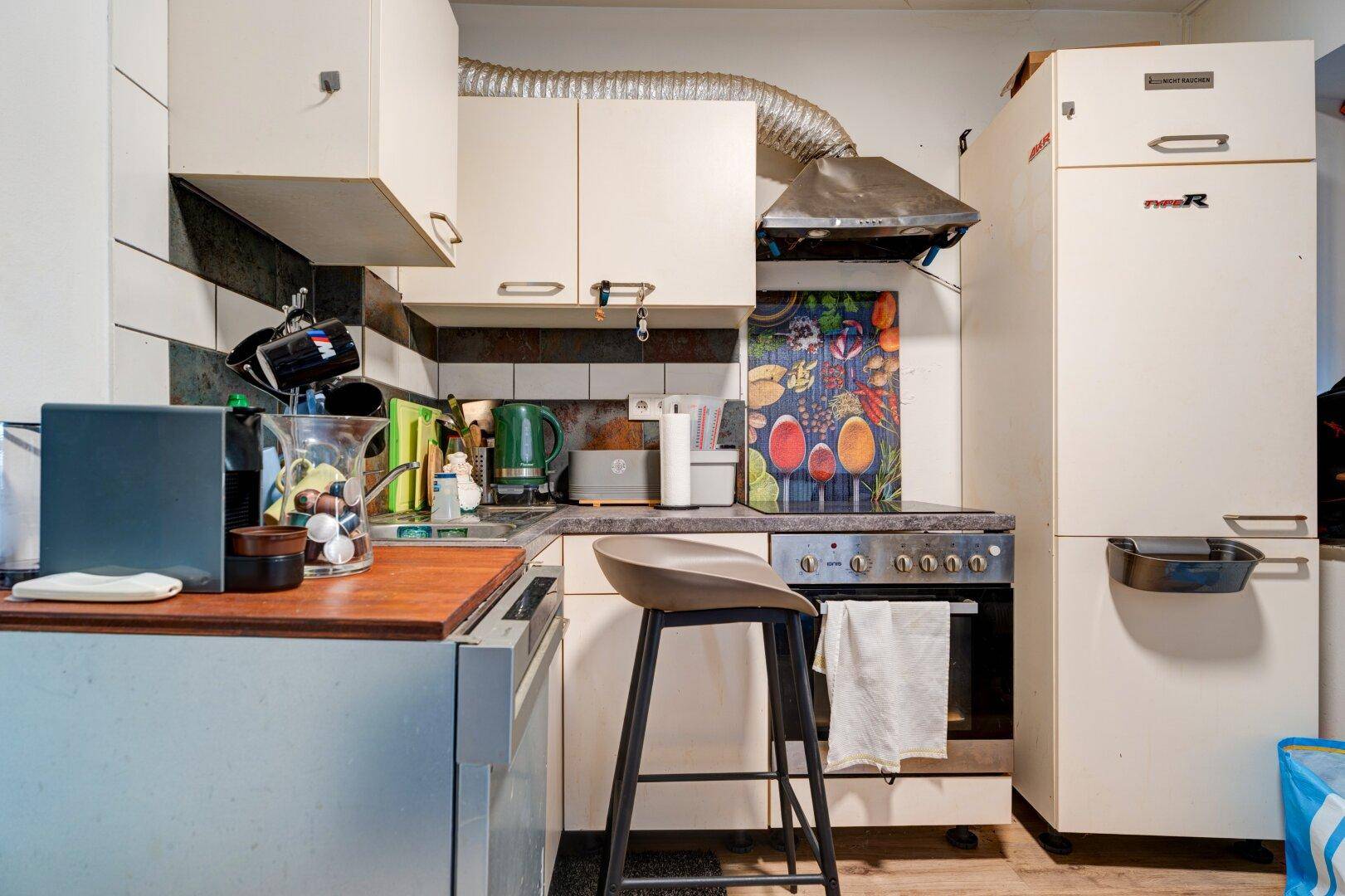 Kompakte Küche mit weißen Schränken, Kochfeld und Kühlschrank, ideal für kleine Räume mit Frühstücksbar.