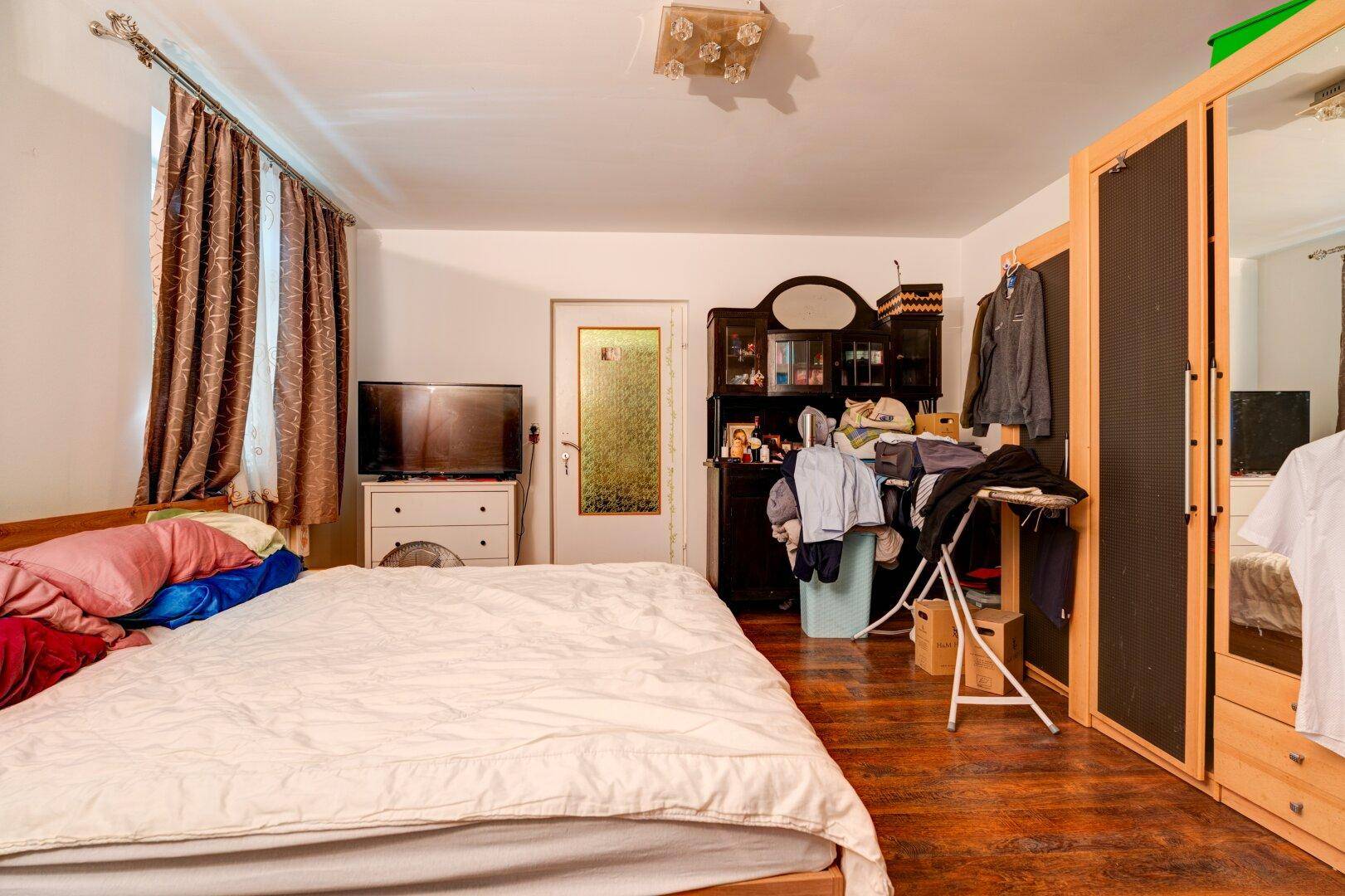 Schlafzimmer mit Doppelbett, dunklem Holzboden und einem Kleiderschrank, der viel Stauraum bietet.