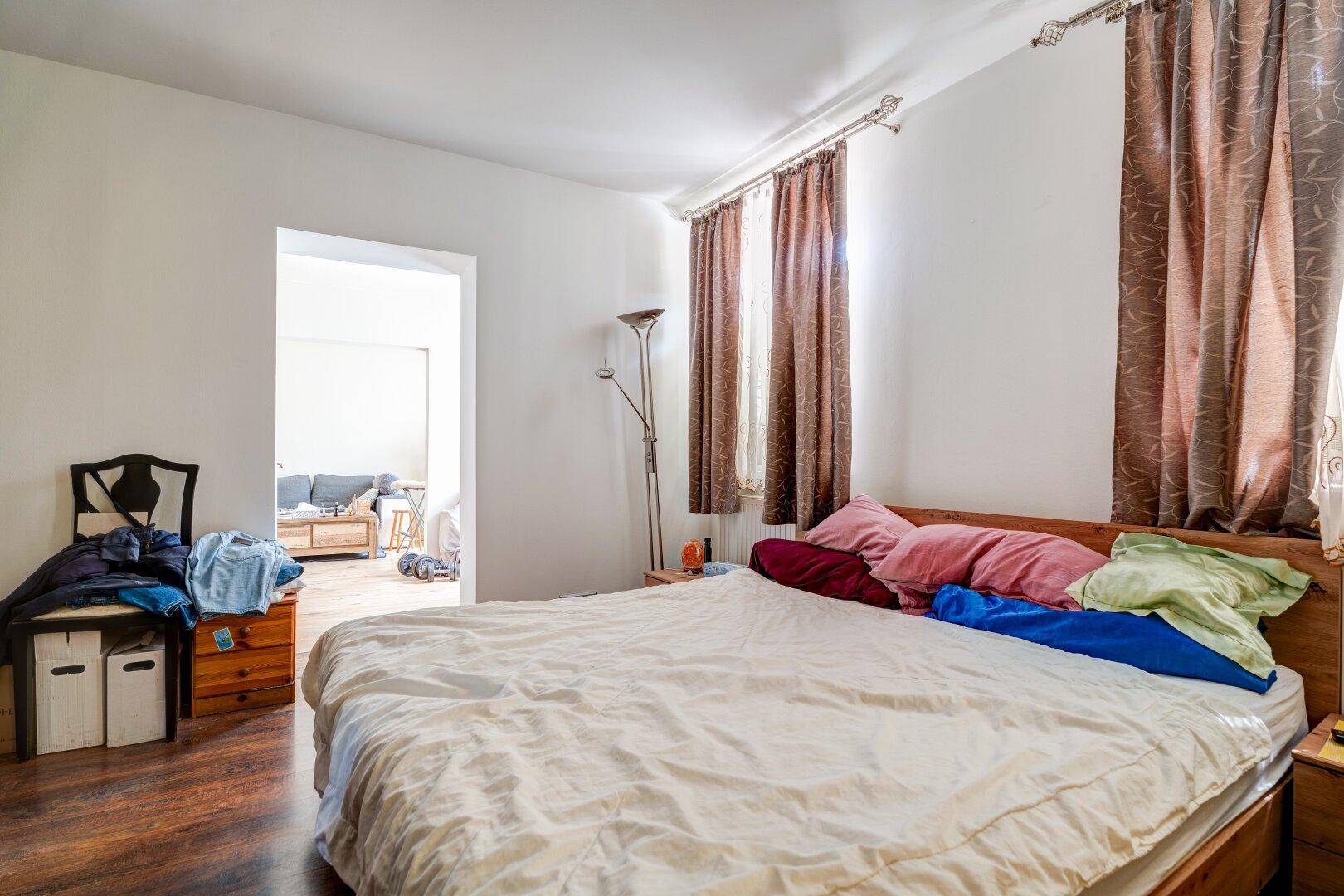 Helles Schlafzimmer mit Doppelbett, Holzboden und Zugang zum Wohnbereich, der eine offene Wohnatmosphäre schafft.