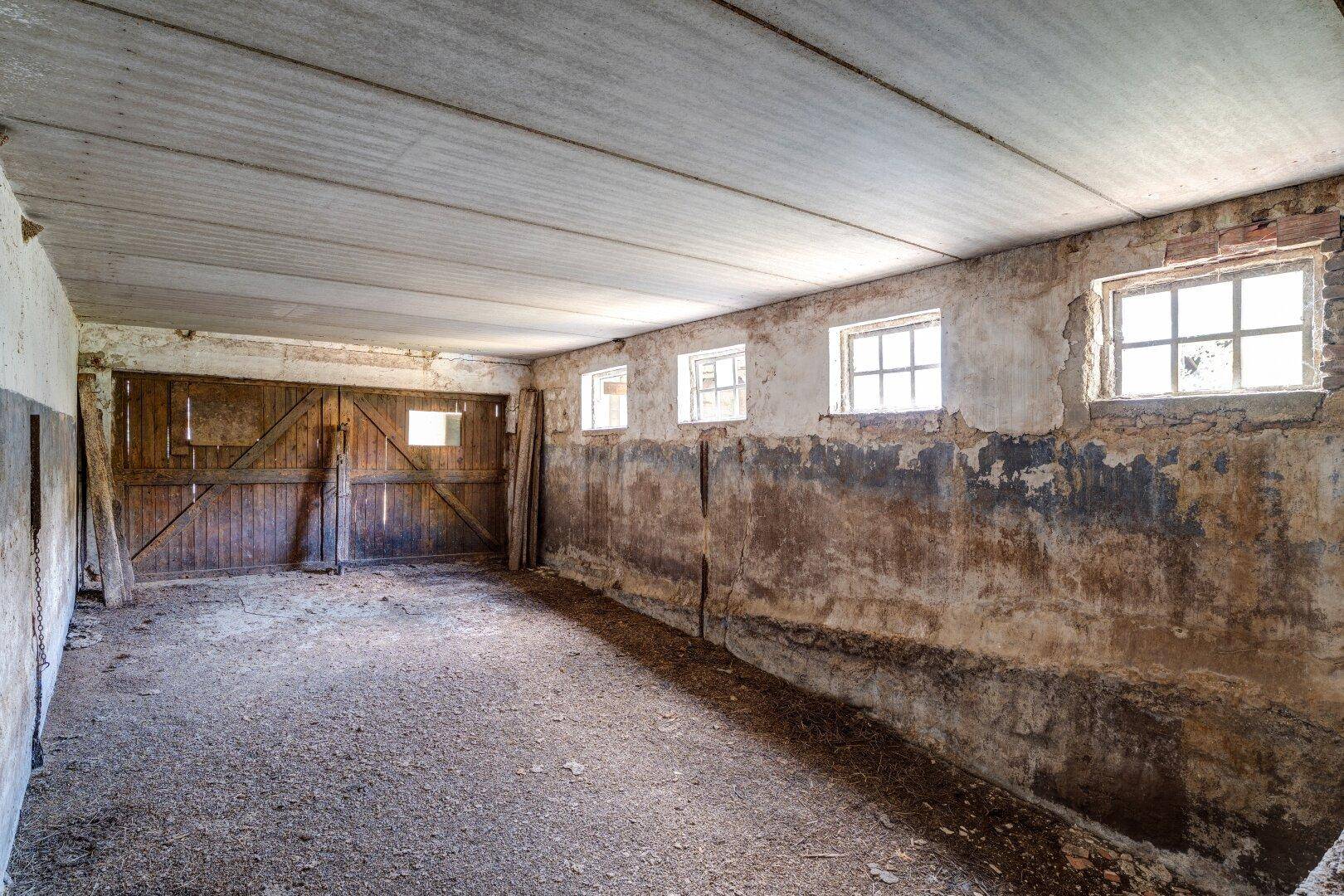 Große, leere Scheune mit Holztoren, kleinen Fenstern und abgenutzten Wänden, die viel Platz bietet.