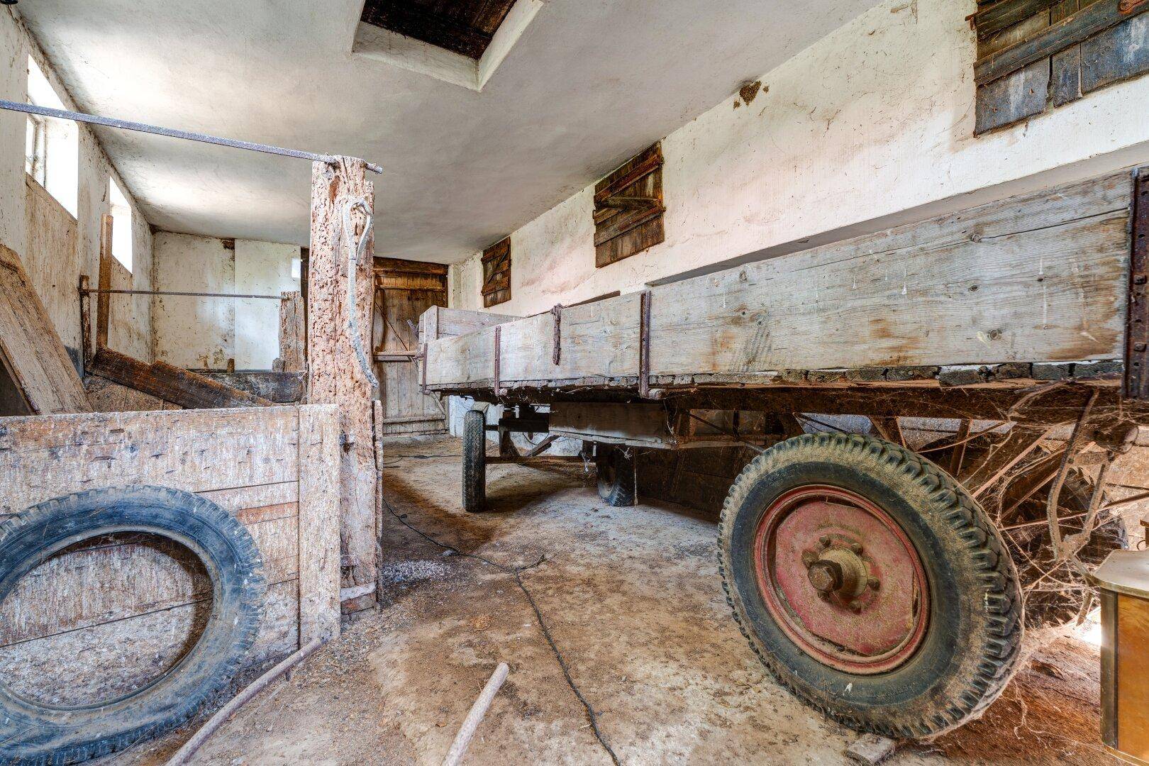 Rustikaler Innenraum mit altem Holzwagen und Reifen, der als Werkstatt oder Lagerraum dient.