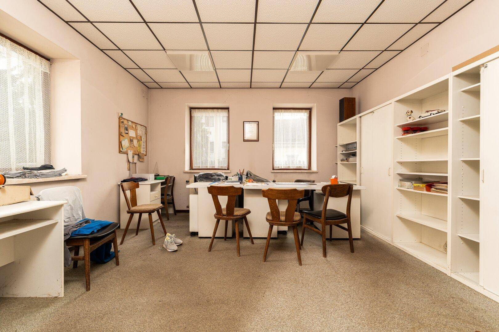 Geräumiges Büro mit Teppichboden, mehreren Arbeitsplätzen und praktischen Regalsystemen.