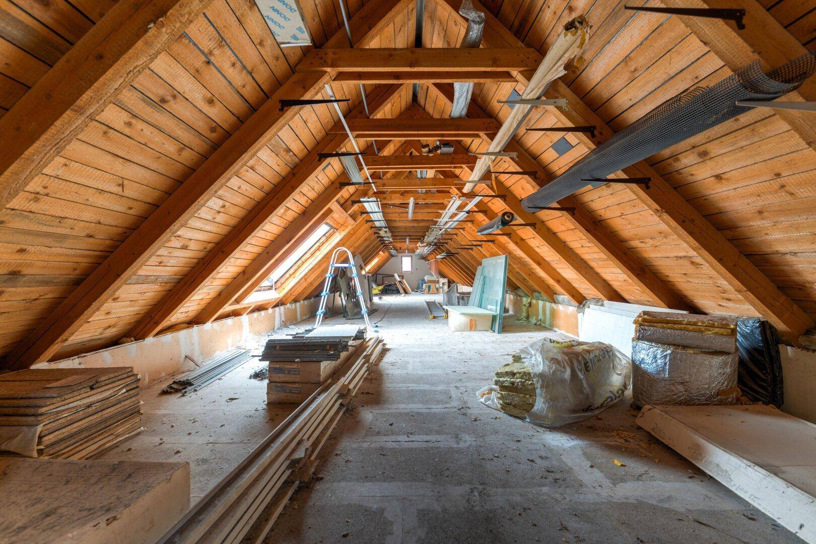 Unausgebauter Dachboden mit sichtbaren Holzbalken und Baumaterialien, bereit für den Ausbau.