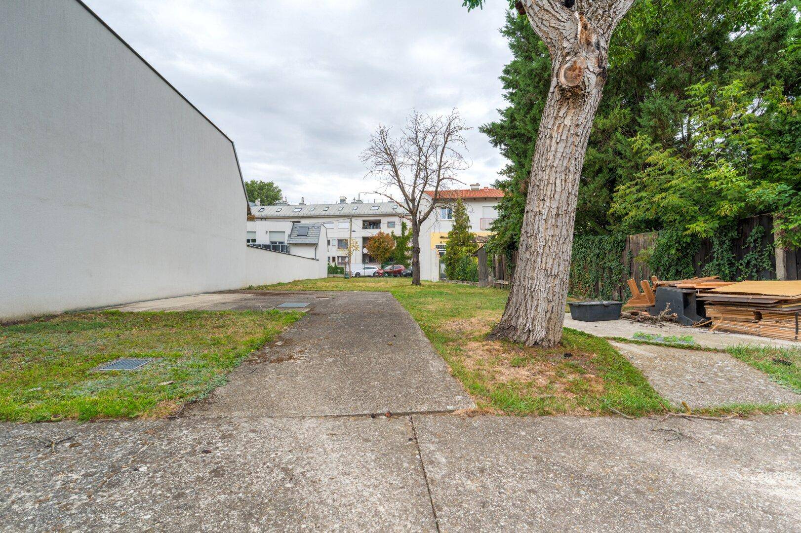 Hinterhofbereich mit Betonweg, Rasenfläche und Bäumen, umgeben von weiteren Gebäuden.
