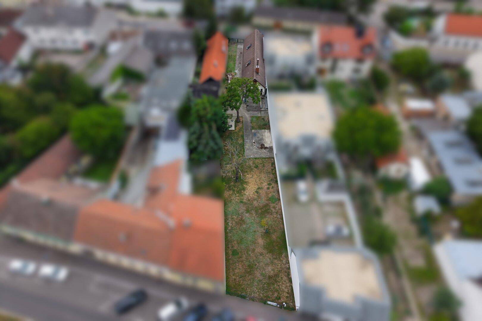 Luftaufnahme des langgestreckten Grundstücks mit umliegenden Gebäuden und viel Grünfläche.
